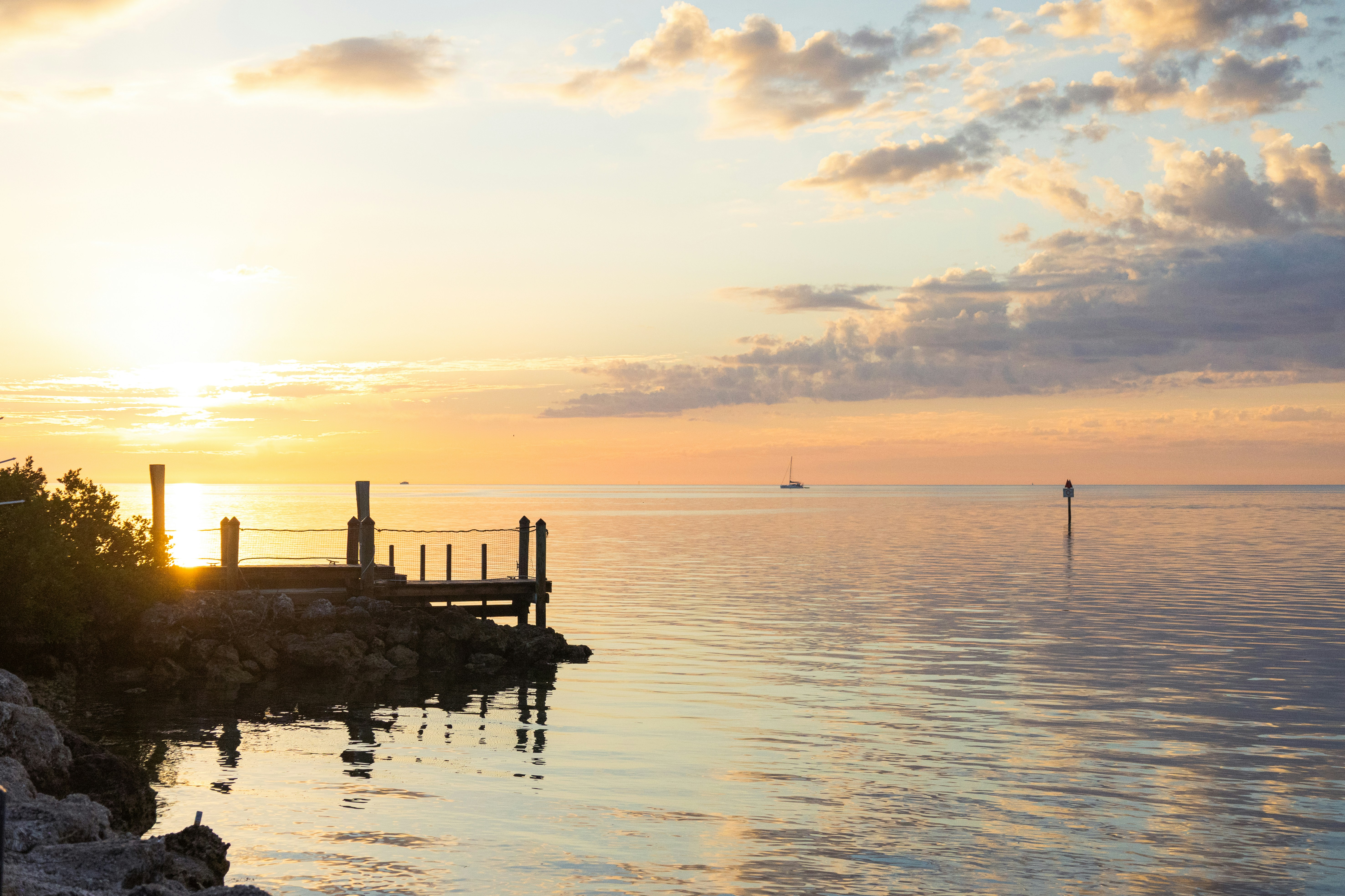 Golden sunset over calm ocean with a small wooden dock.