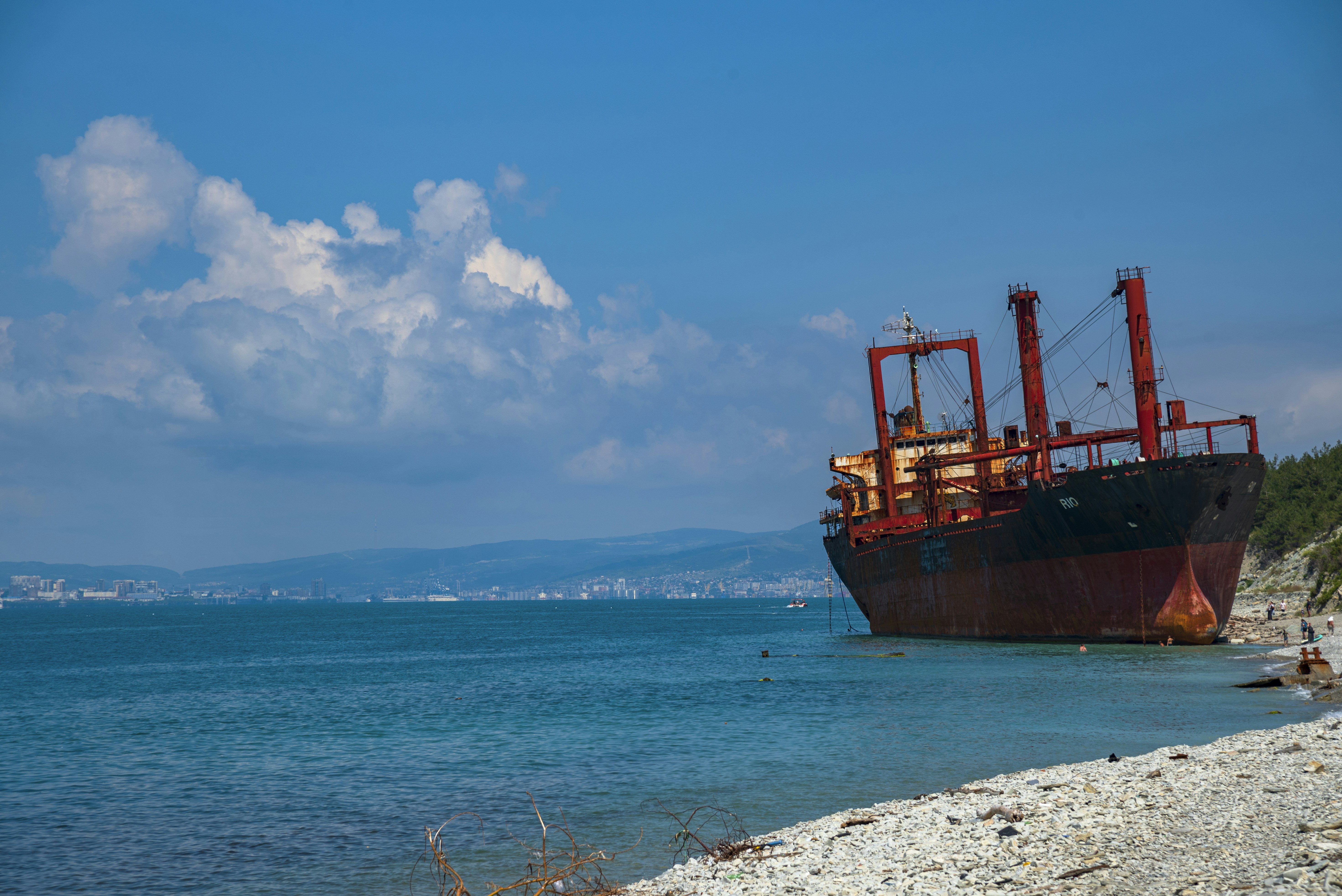 Rusty cargo ship stranded on a sunny pebble beach.