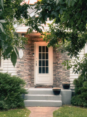 A white front door with stone siding and green foliage.