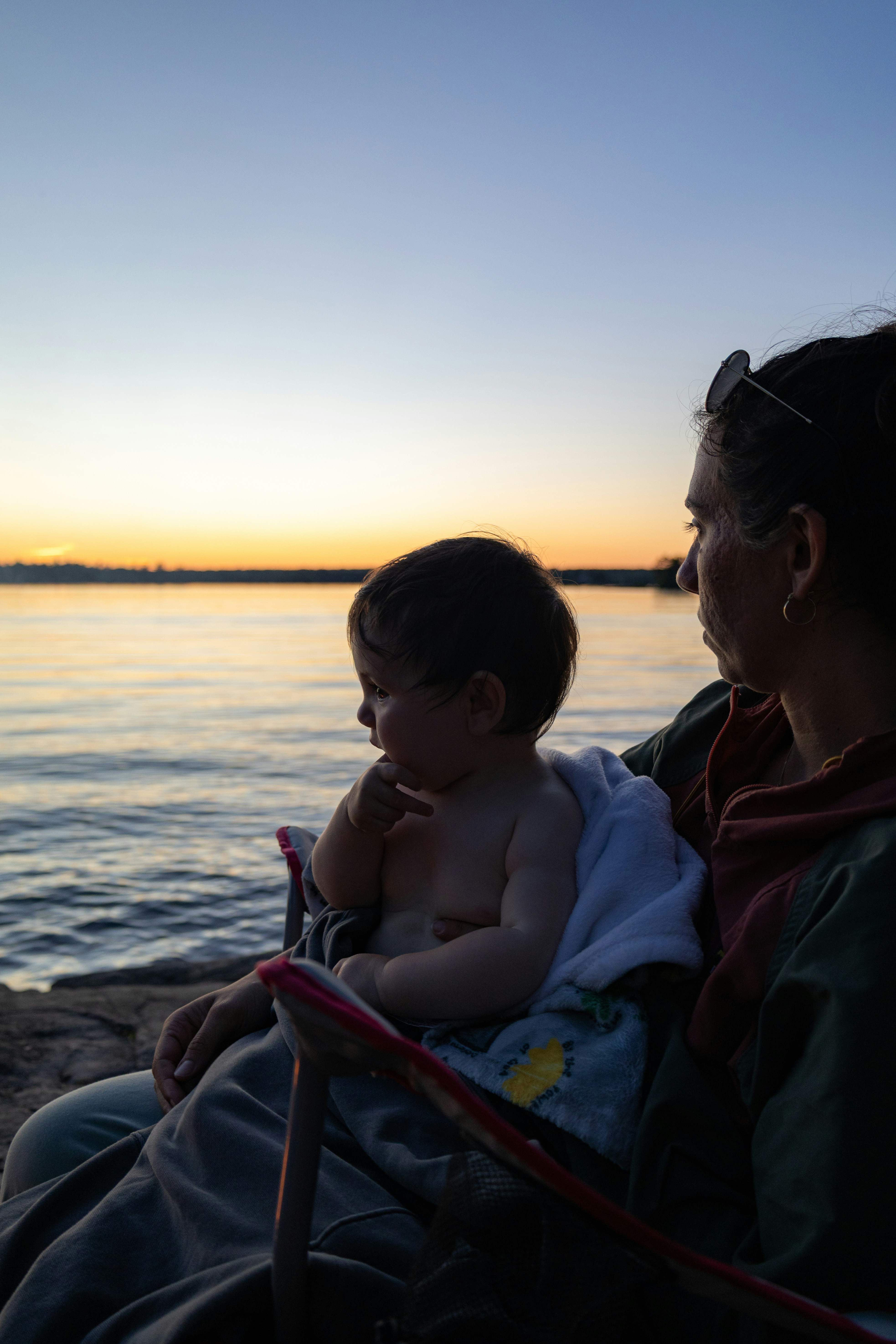 Une femme tenant un bébé regardant le coucher du soleil au-dessus de l’eau.