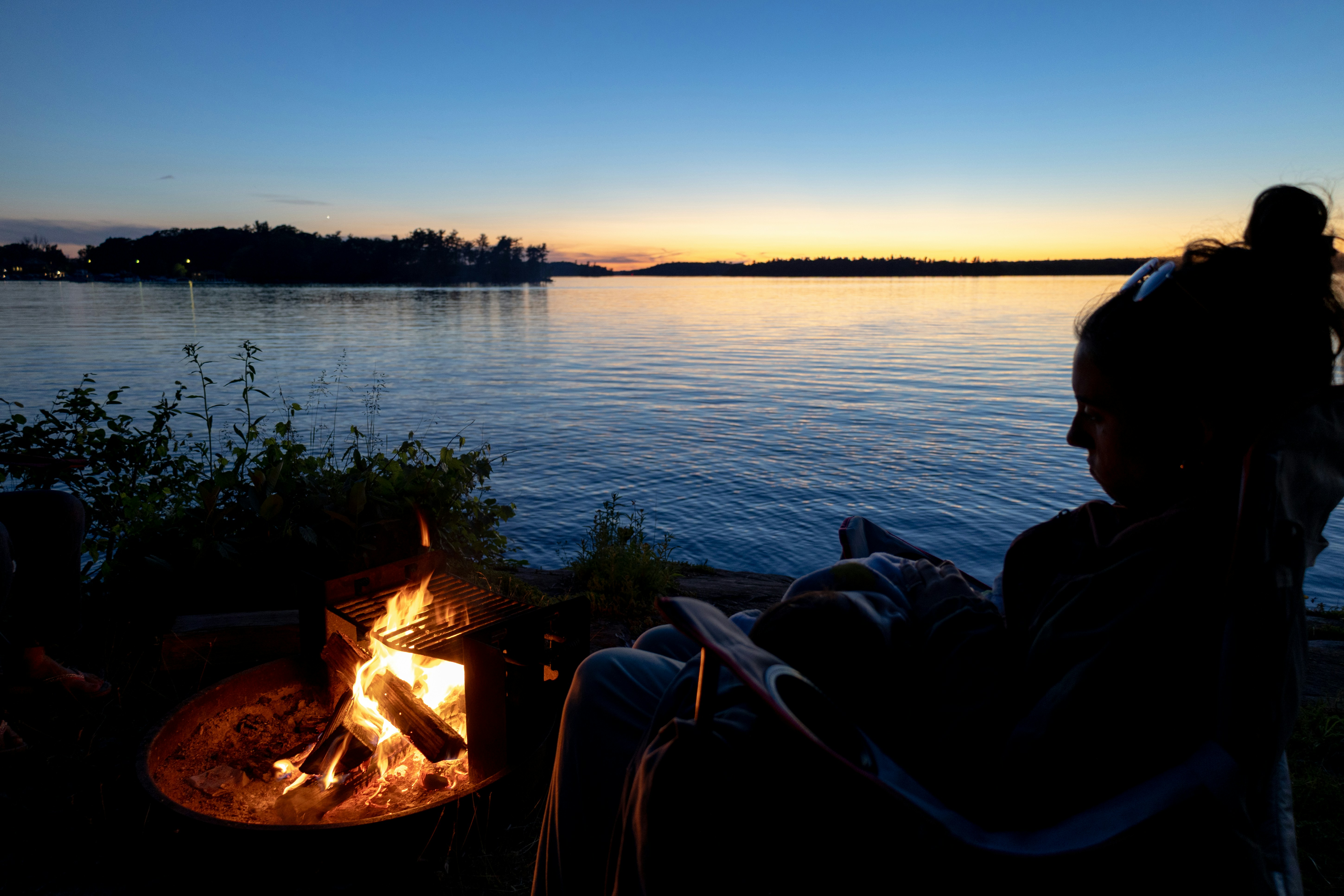 Personne près du feu de camp regardant le coucher de soleil au-dessus du lac.
