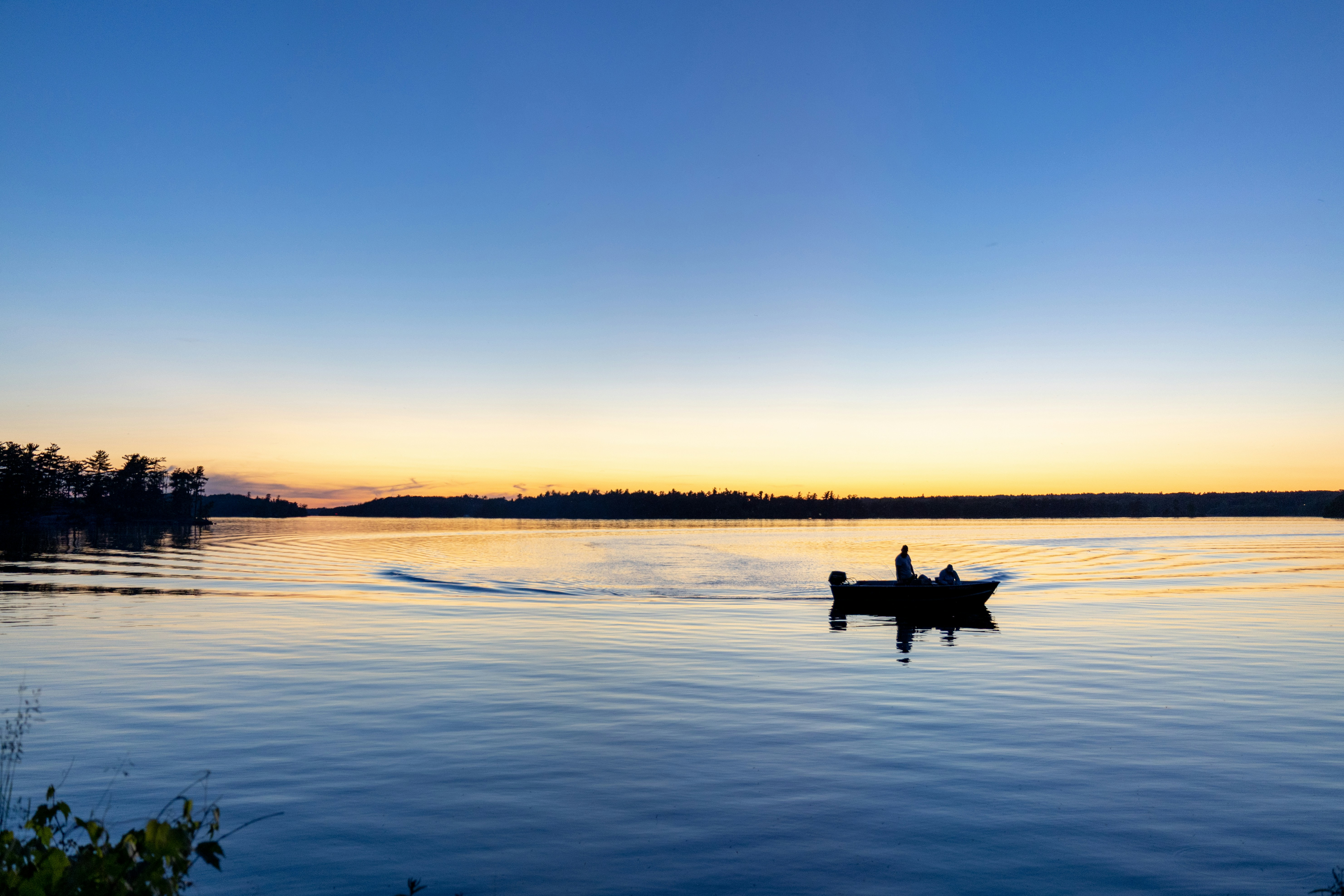Un bateau avec des gens sur un lac calme au coucher du soleil.