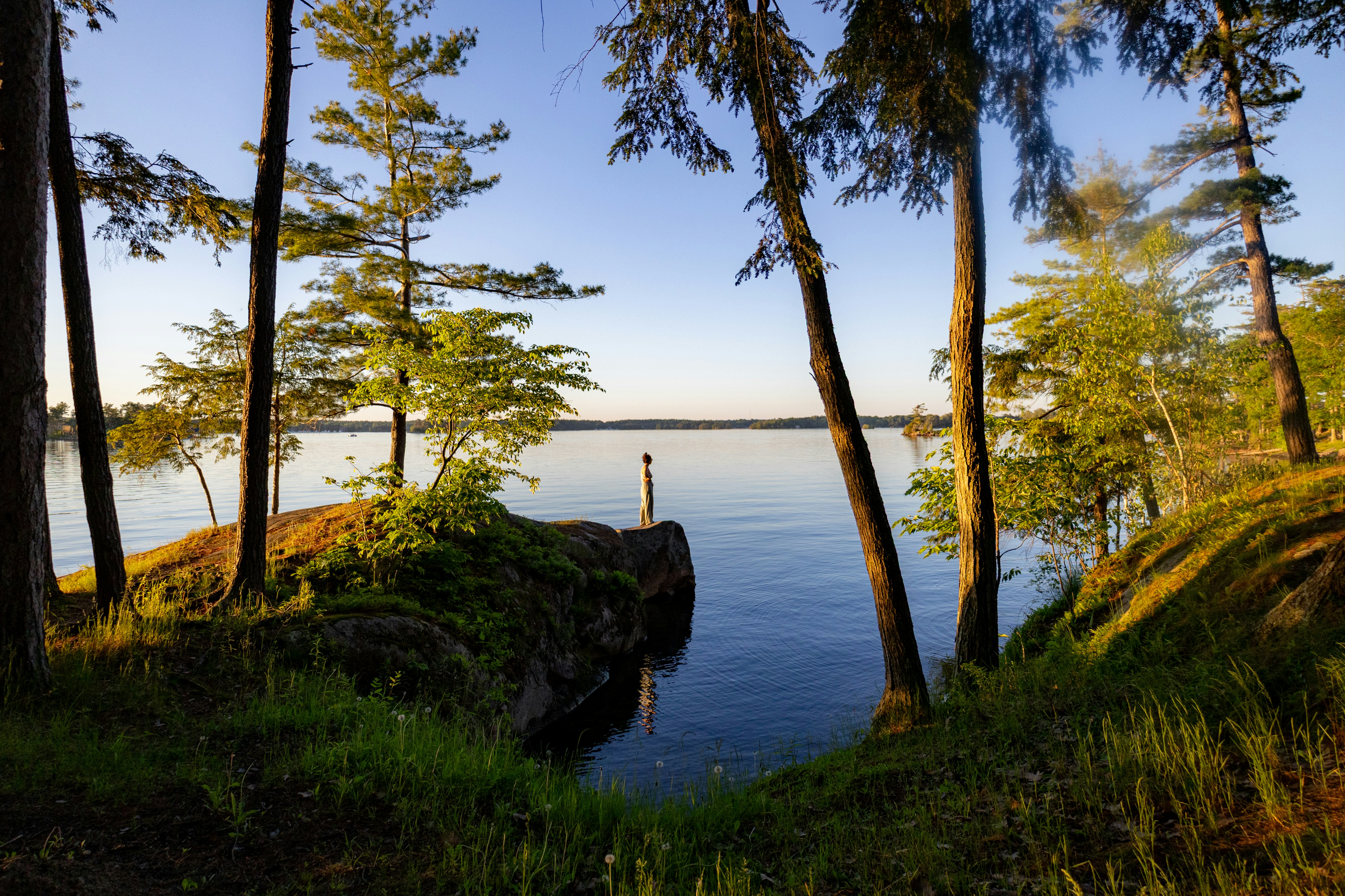 Personne sur un affleurement rocheux près d’un lac encadré d’arbres.