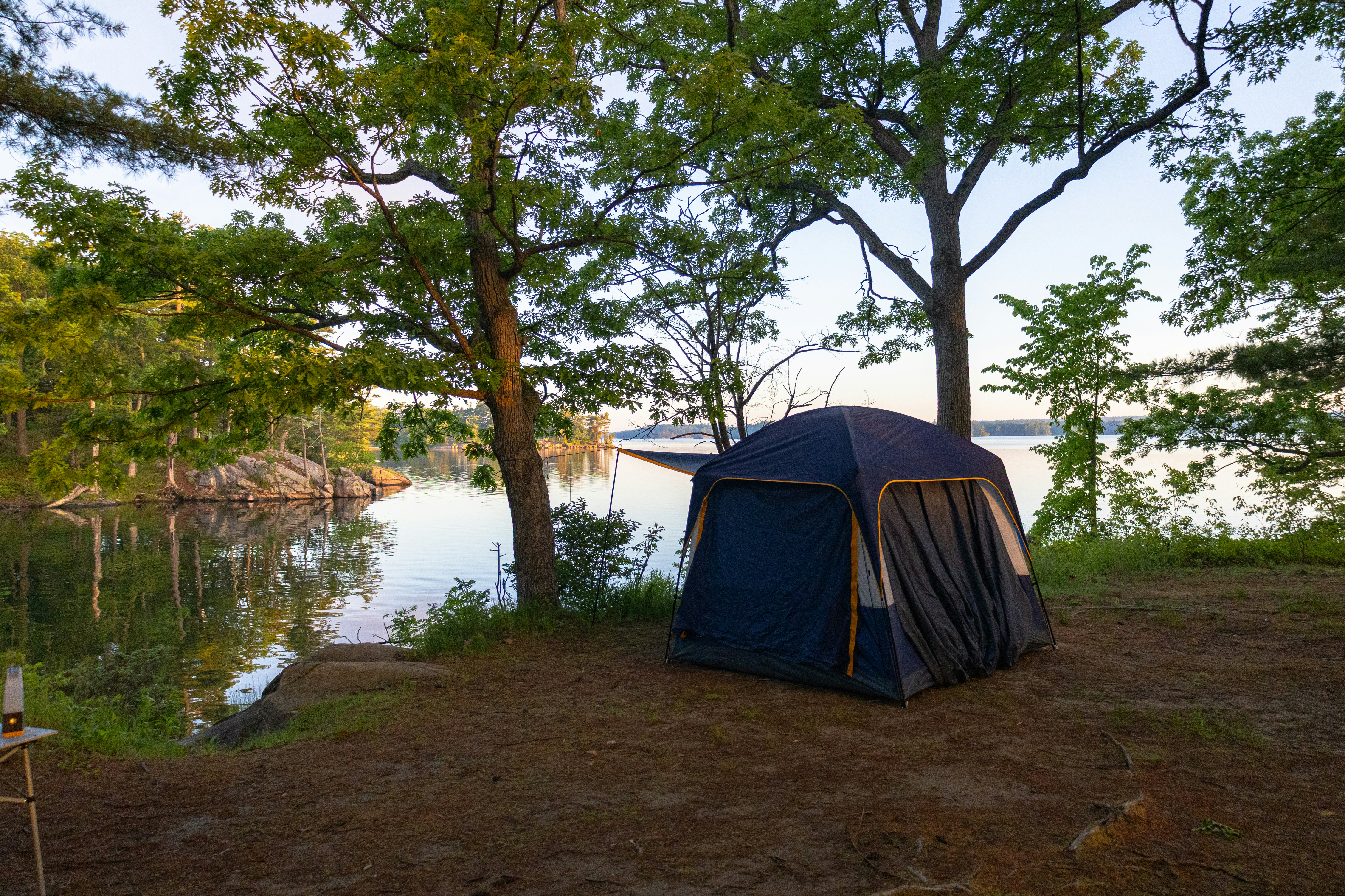 Tente bleue dressée près d’un lac calme avec des arbres verts.