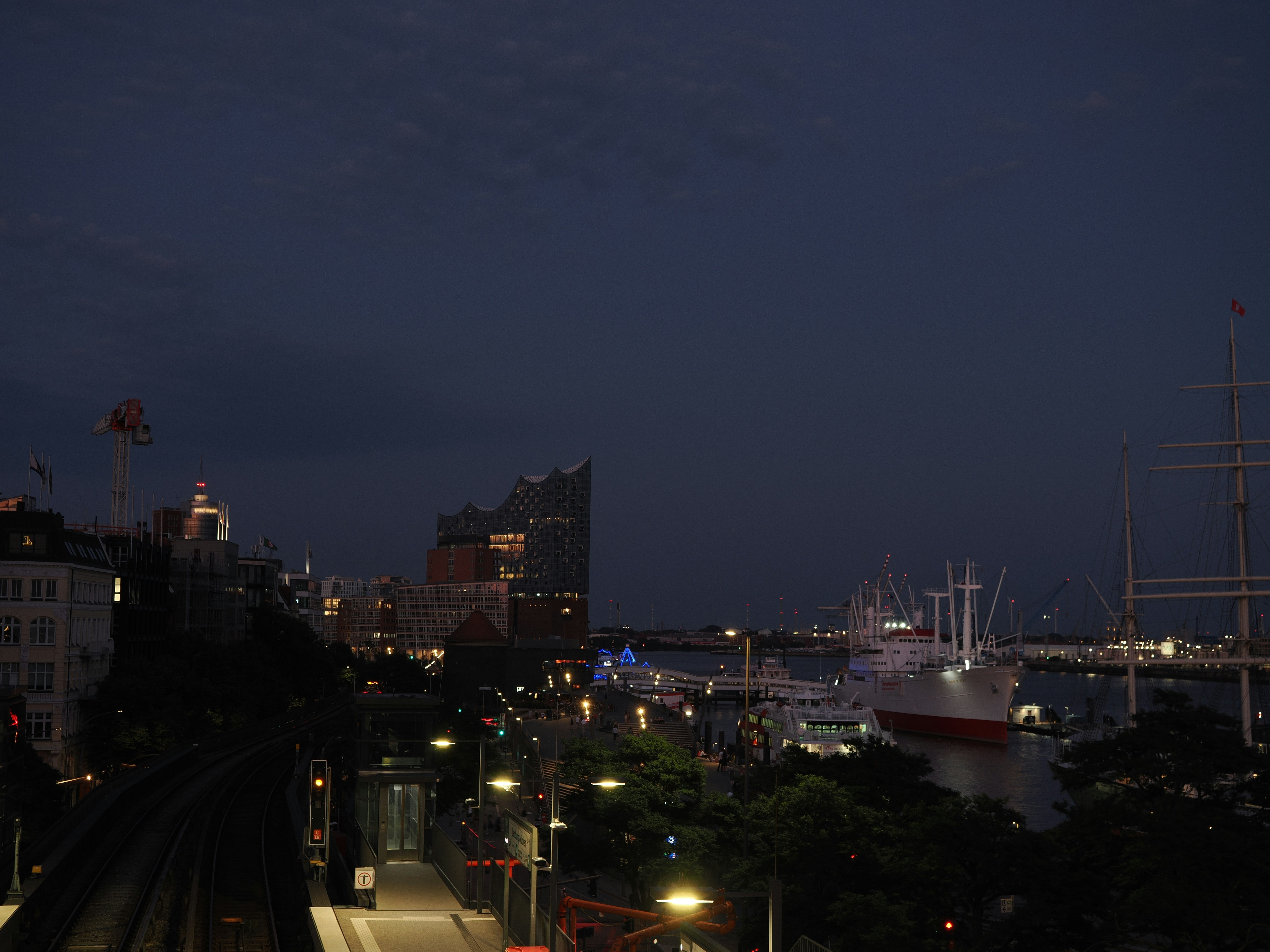 City harbor at dusk with ships, buildings, and train tracks.