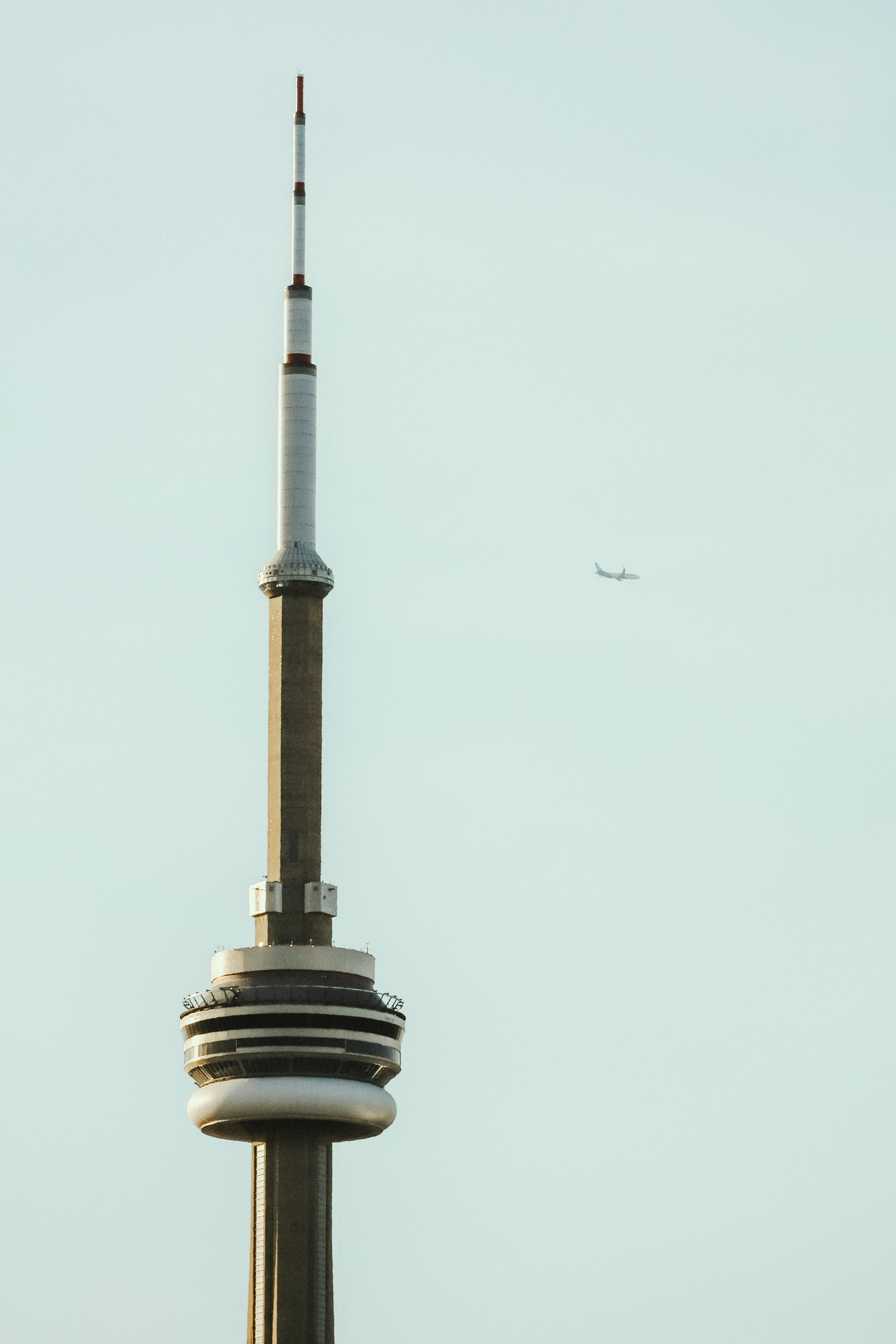 Iconic tower and airplane against a clear, pale sky