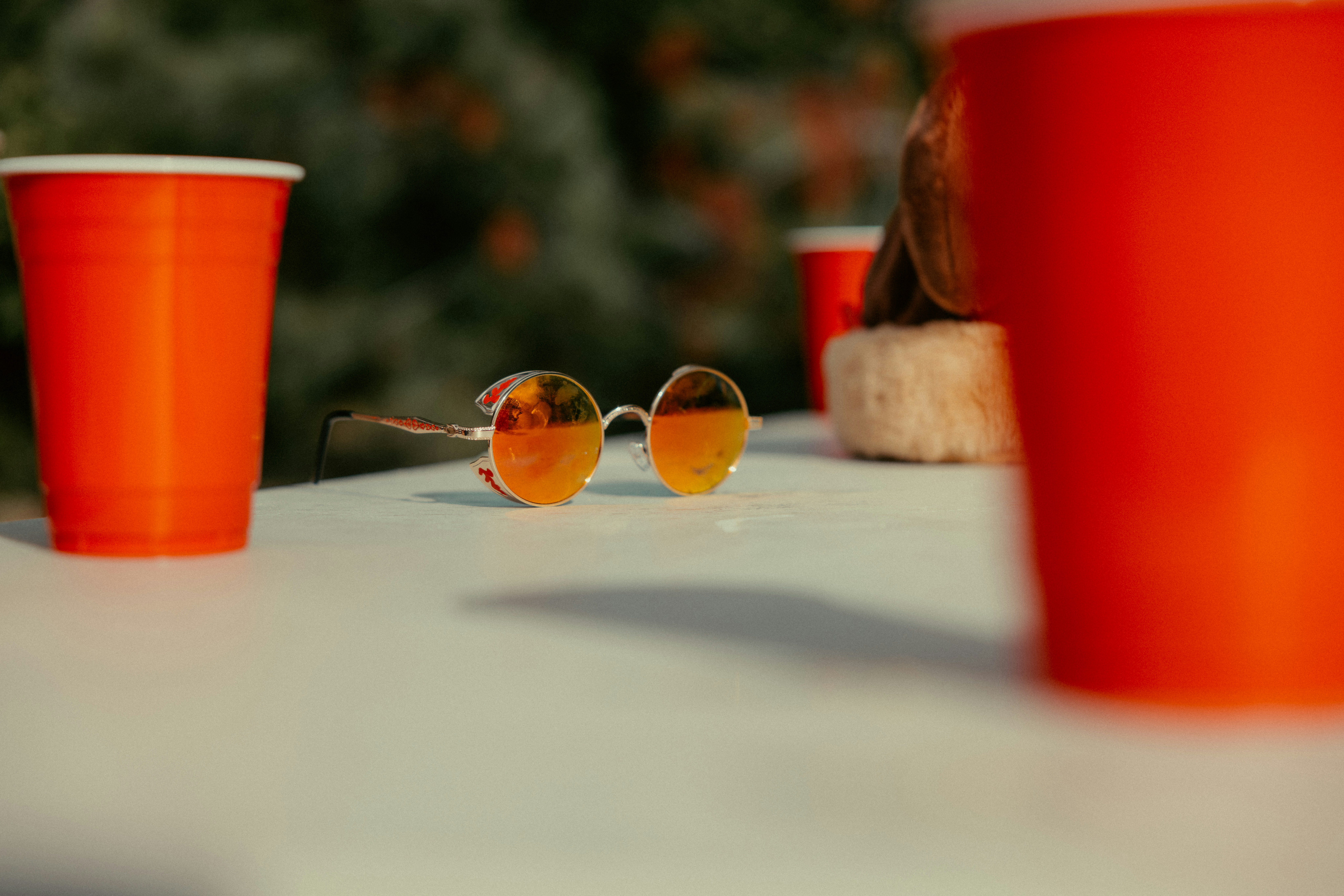 Red cups and orange sunglasses on a white table.