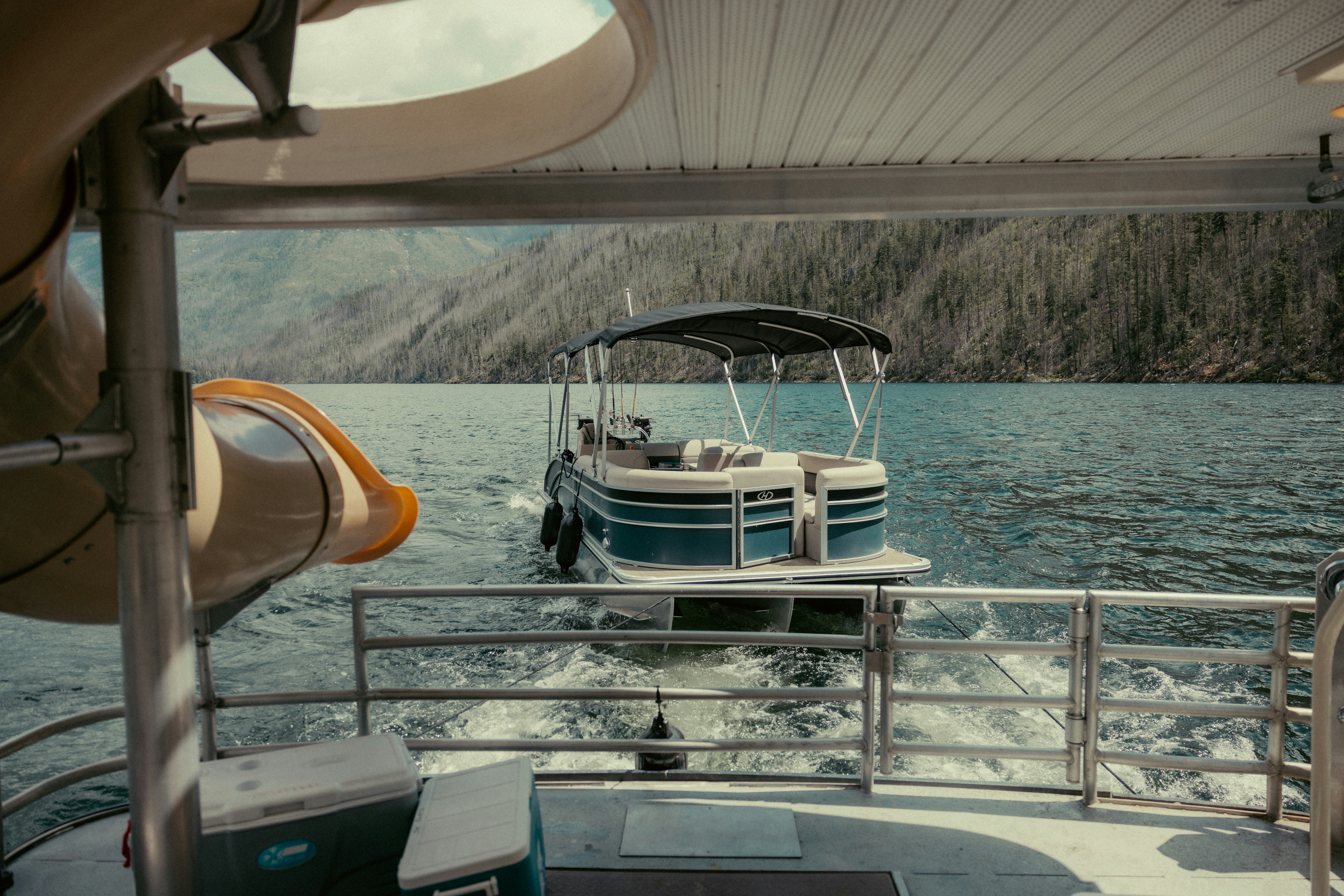 A boat tows another boat on a lake near mountains.
