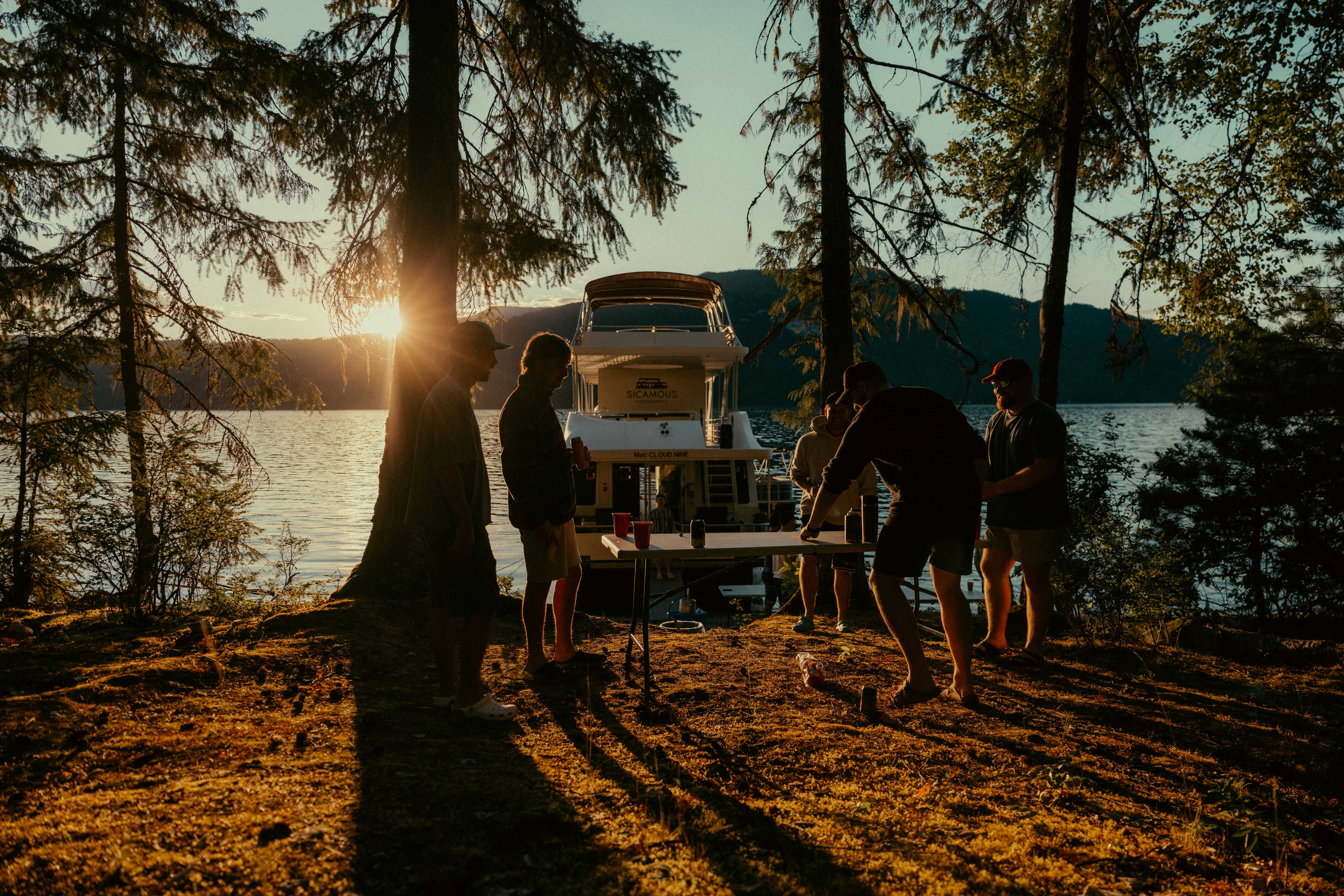 People play by a lake with a boat at sunset.