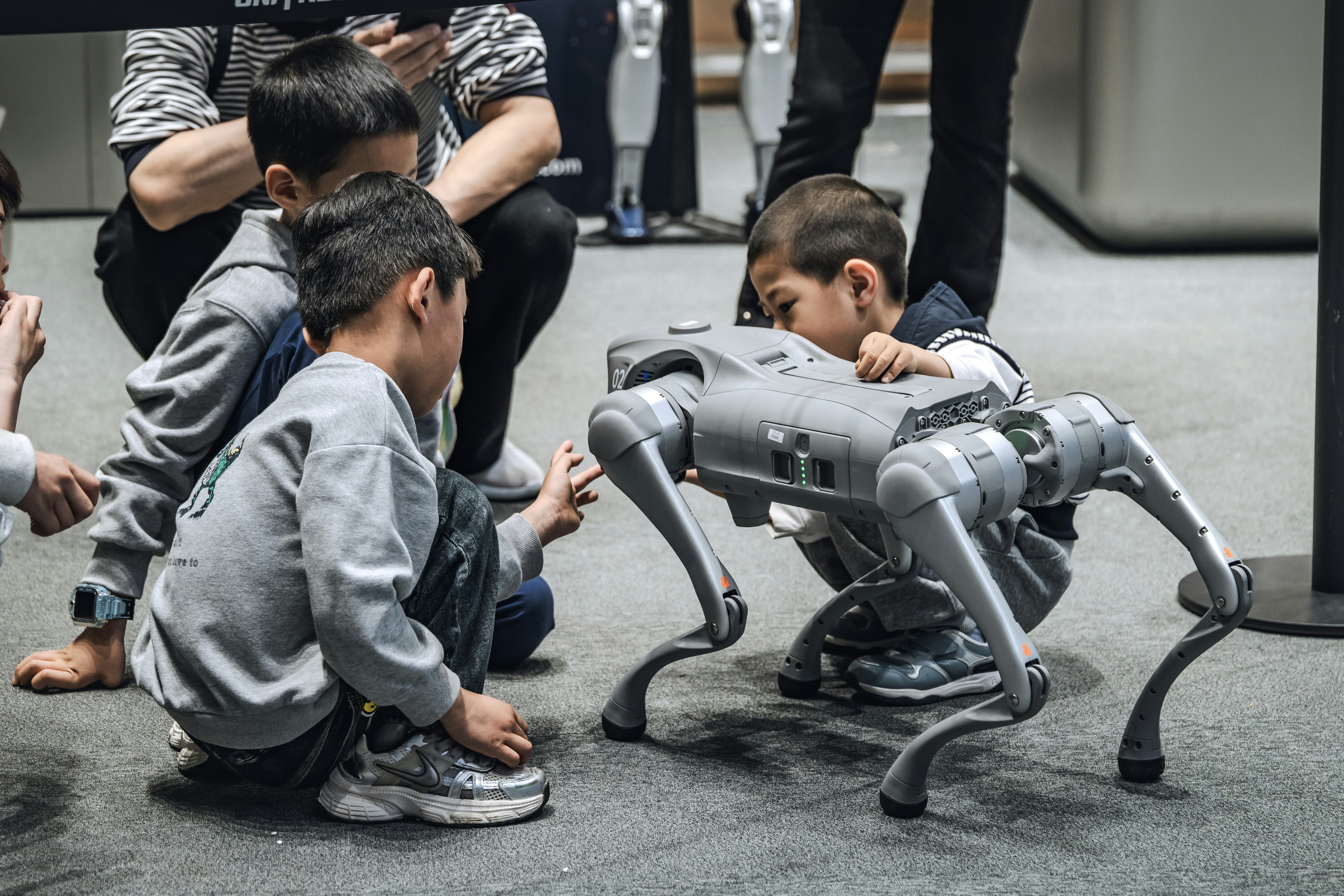Children gather around a robotic dog, observing it closely.
