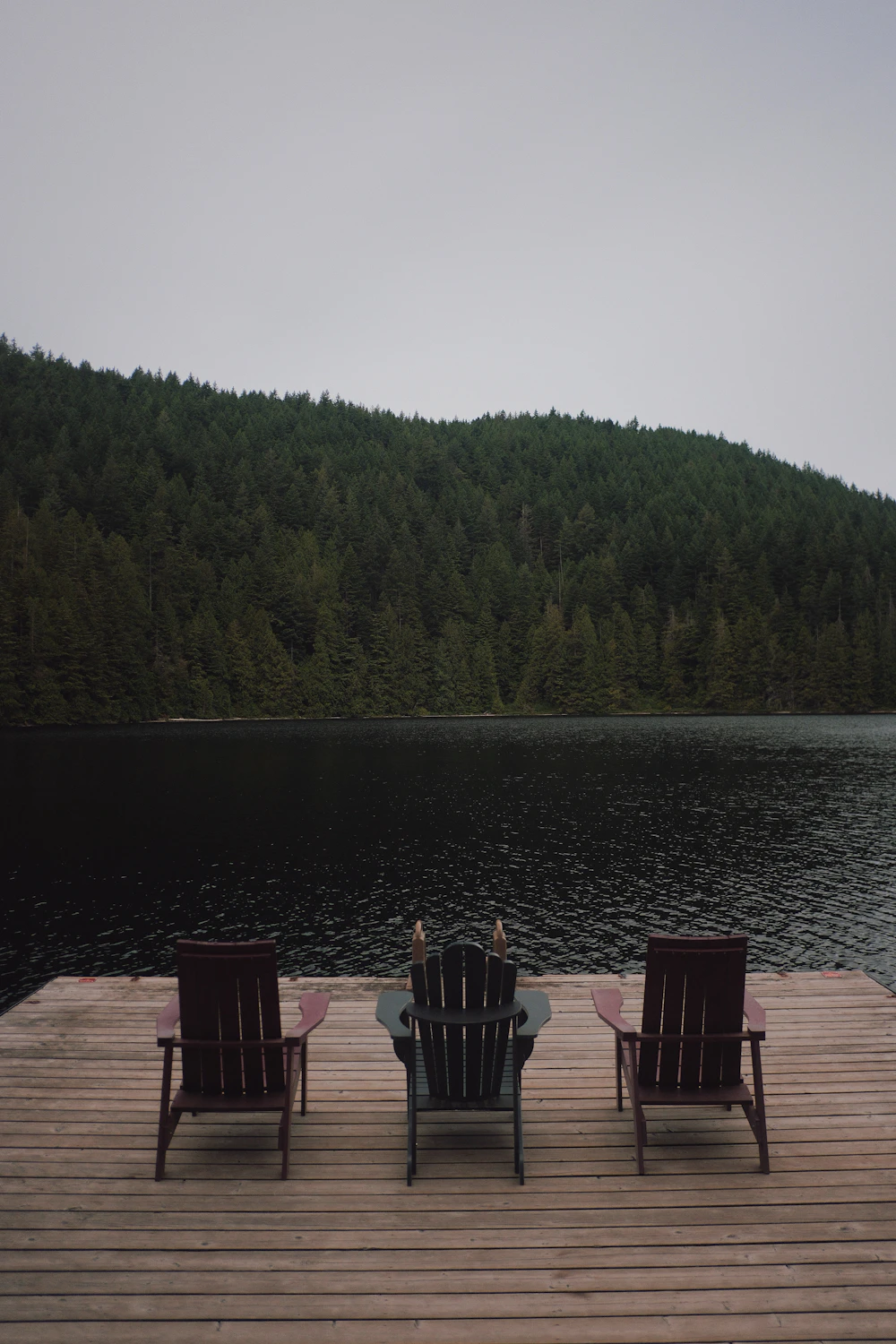 Wooden chairs on a dock by a lake and forest