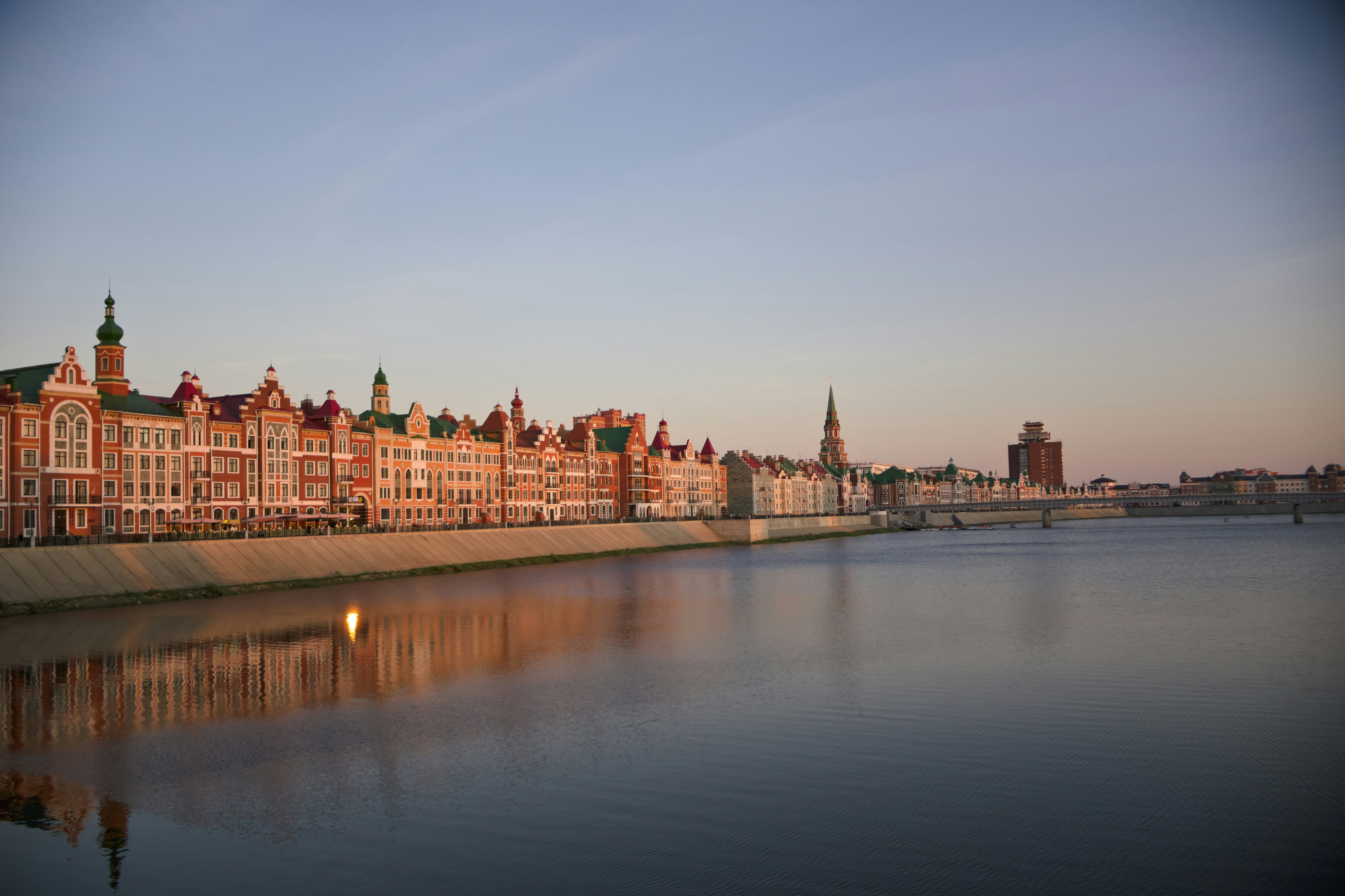 Historic buildings line a riverbank under a clear sky.