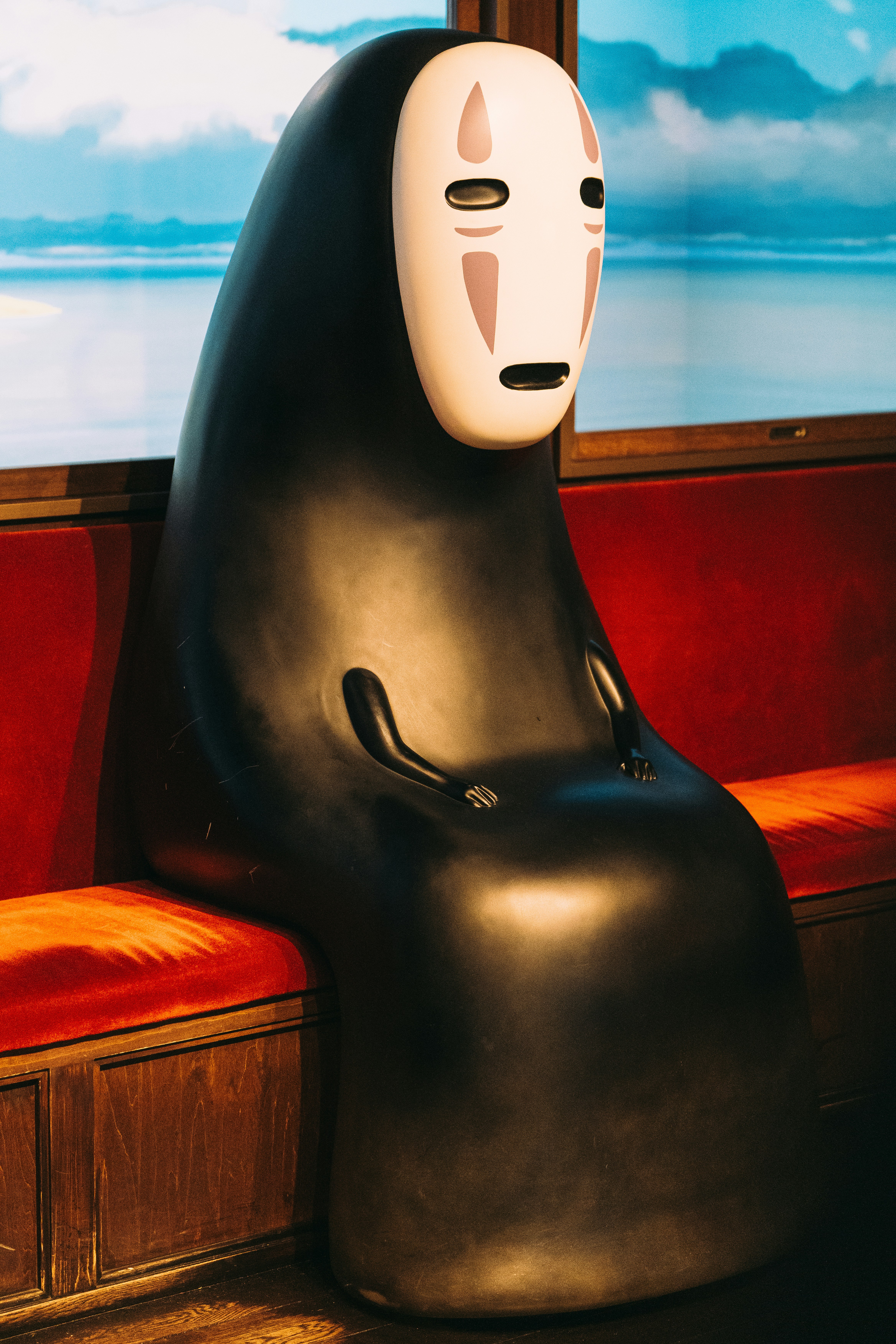 No-face character from spirited away sitting on a red bench