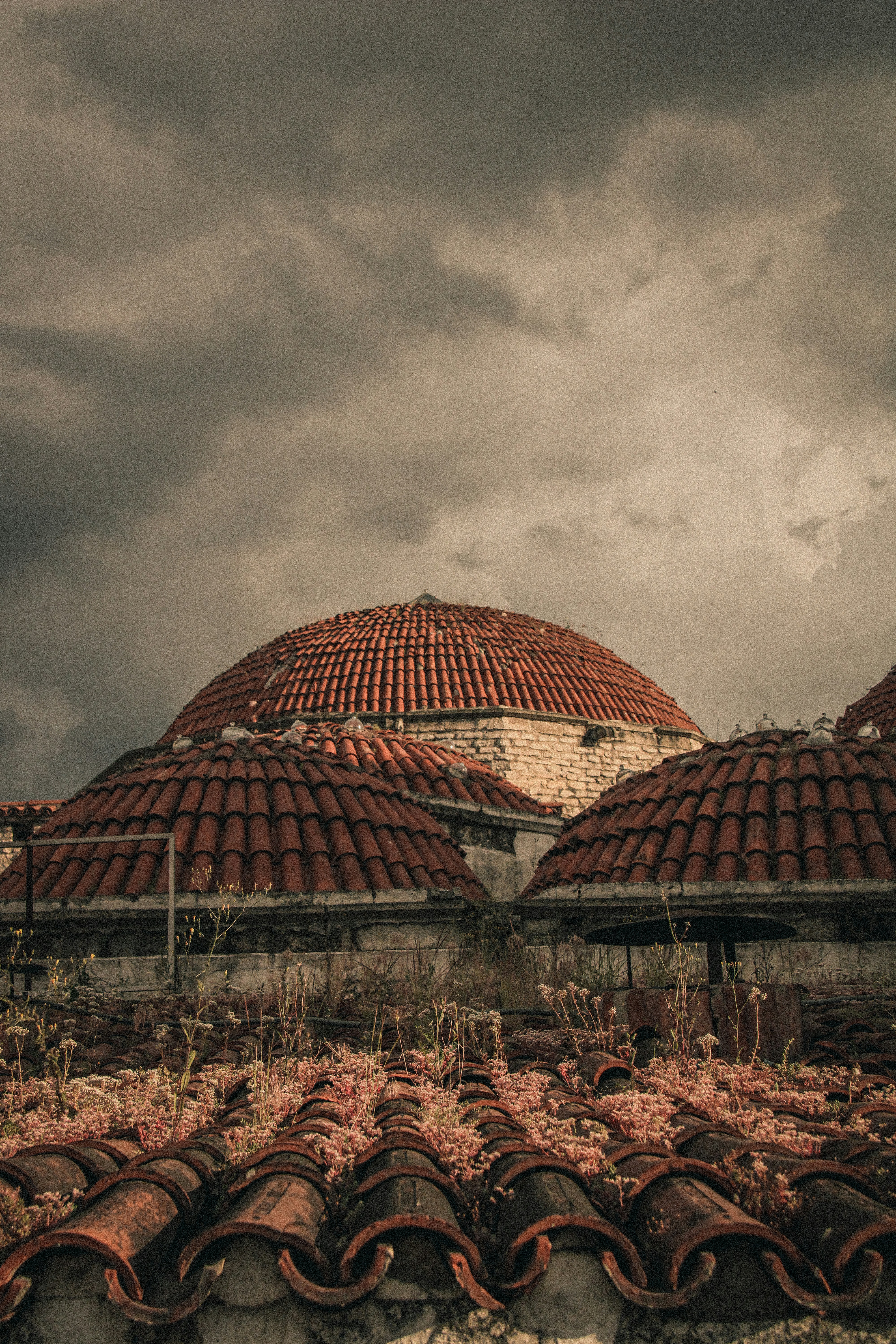 Old red-tiled roofs and a dome under a cloudy sky.