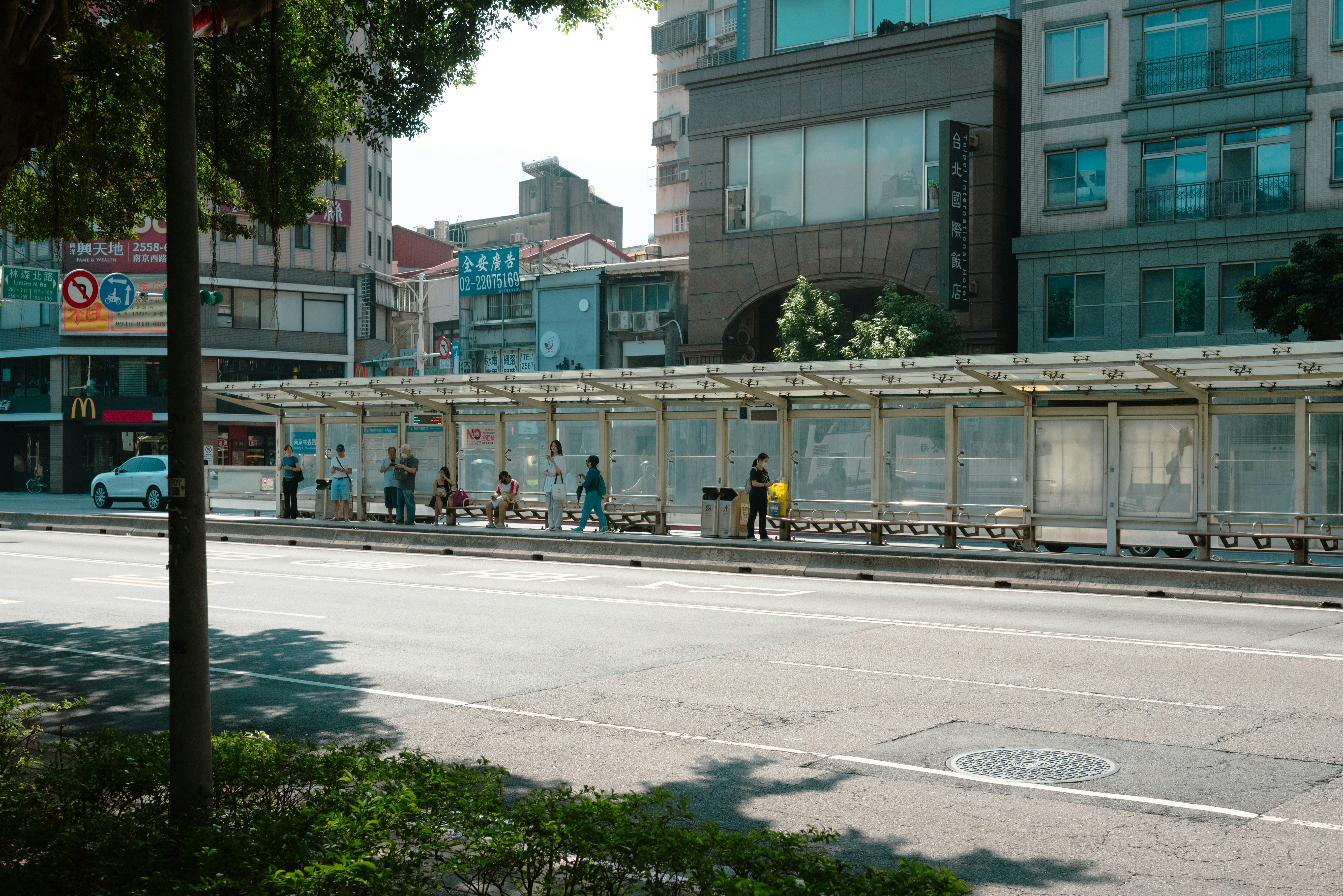 Long bus shelter with people waiting beside a wide road
