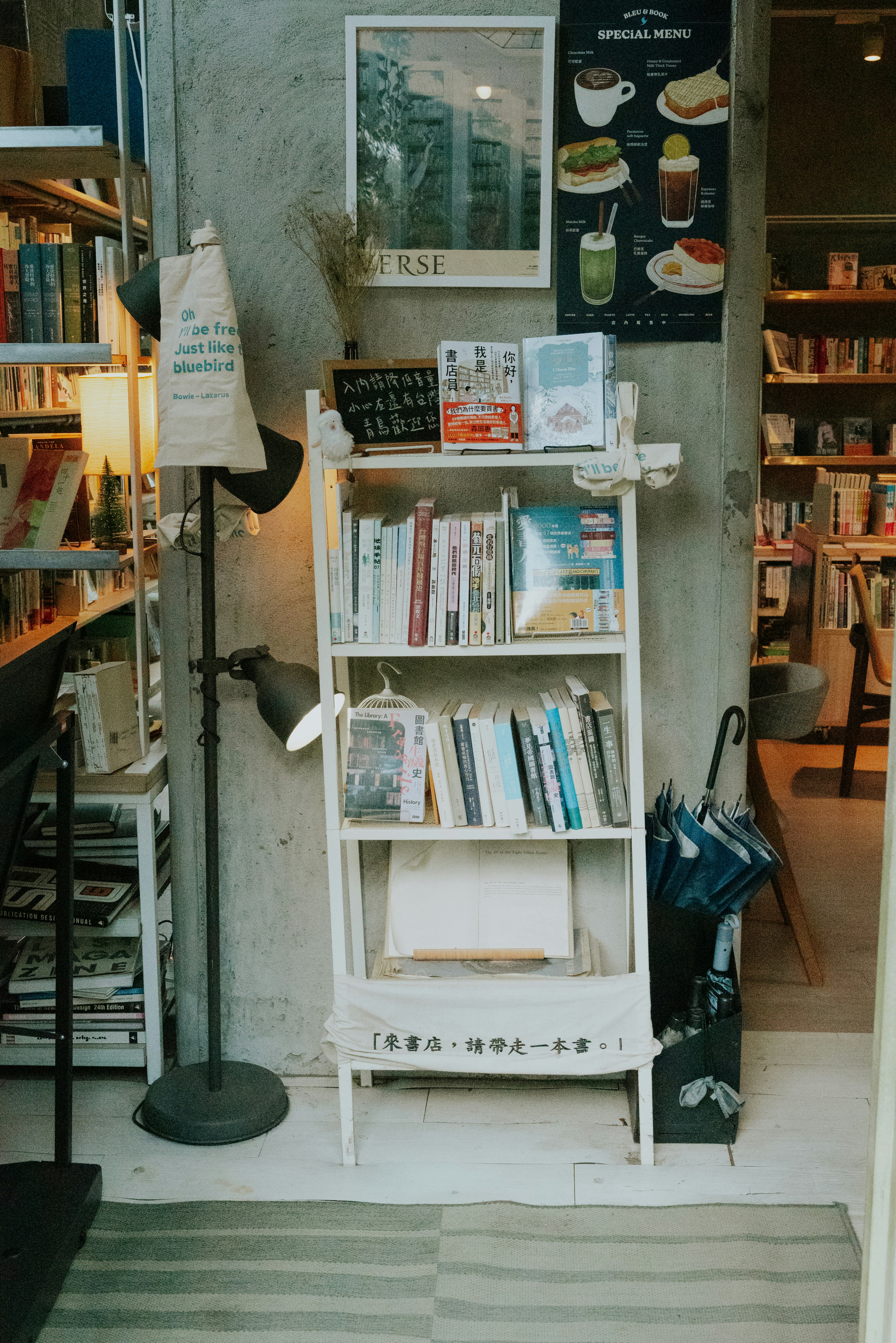 A white bookshelf filled with books beside a floor lamp in a bookstore