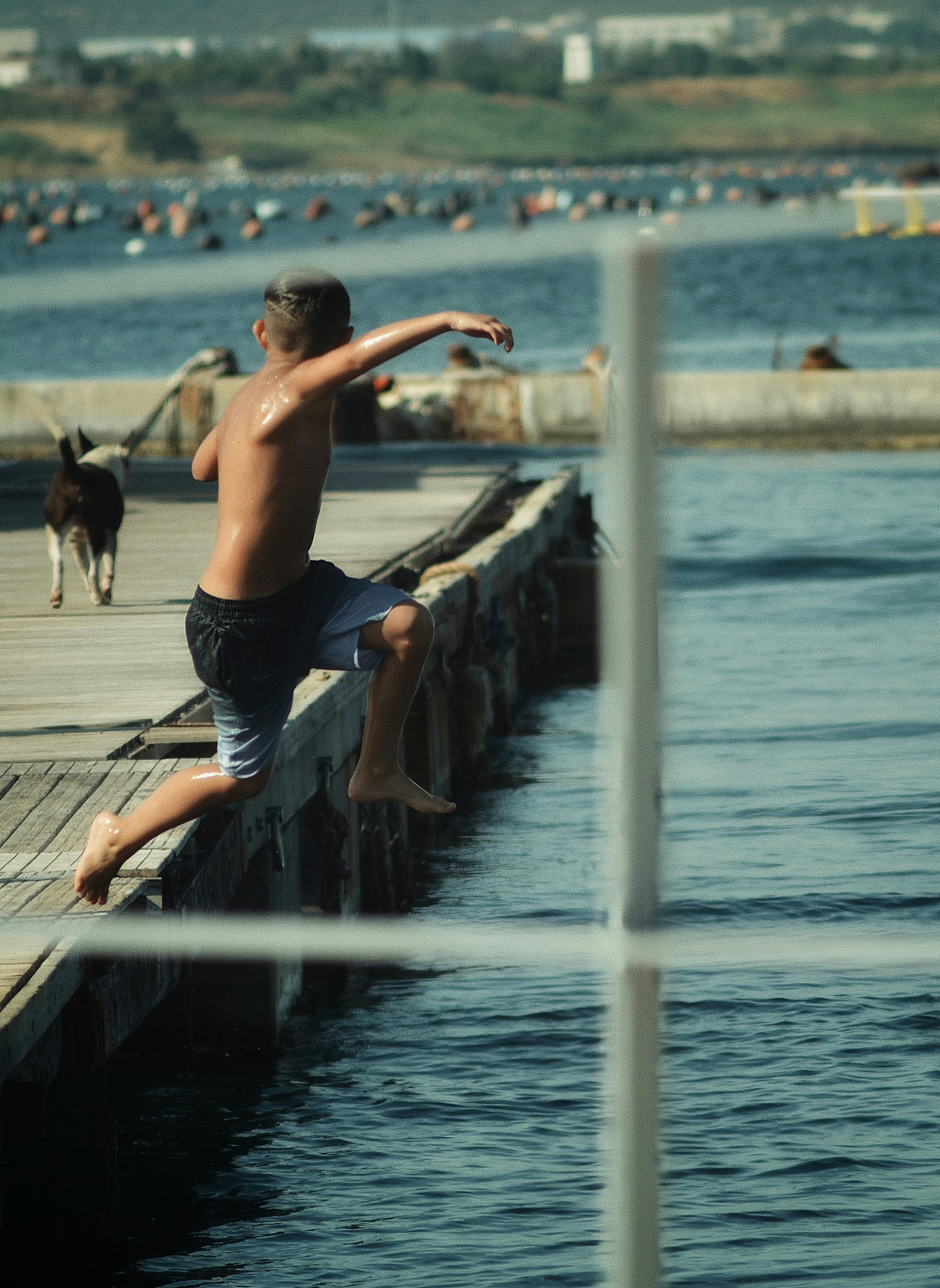 Young boy leaps from a wooden pier into the sea