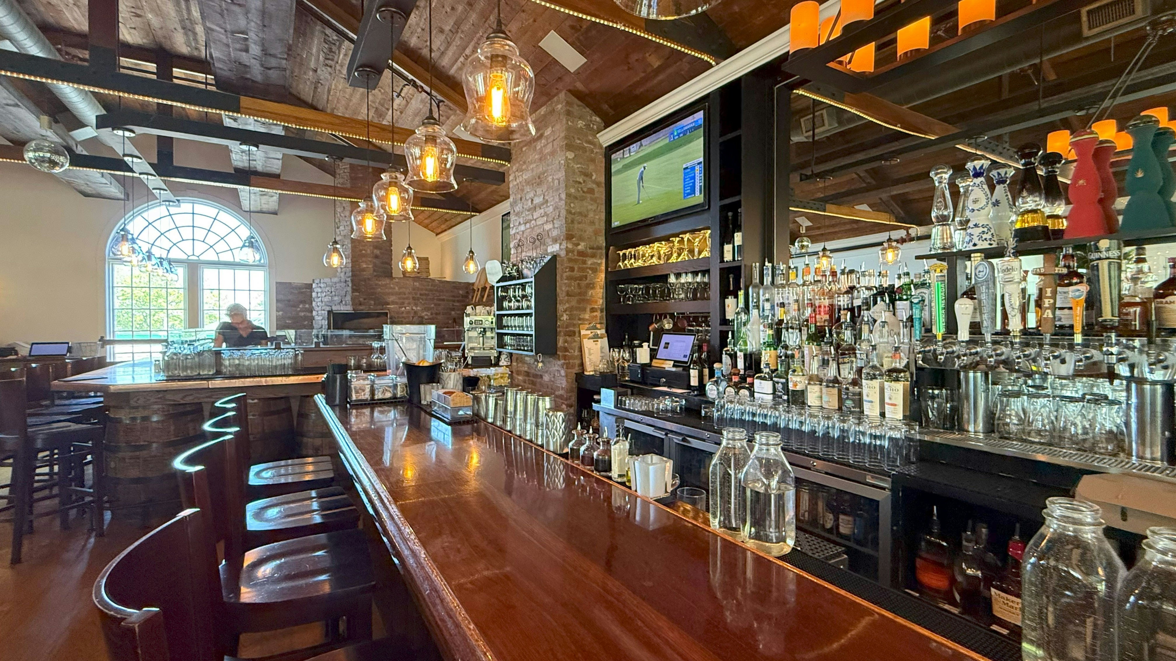 Inviting bar interior with wooden counter, stools, and bottles.