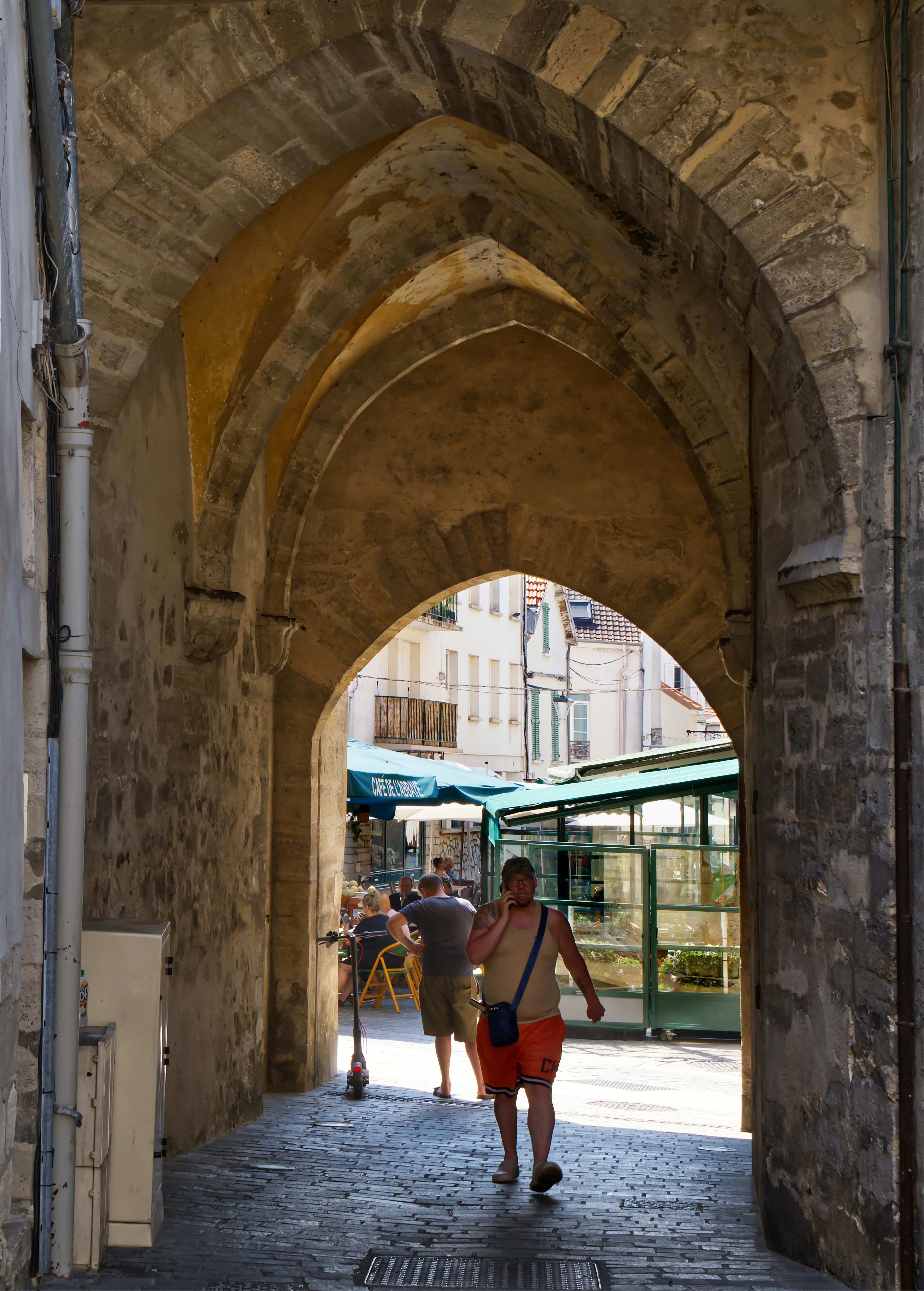 Arco histórico de piedra con gente caminando hacia un mercado luminoso.