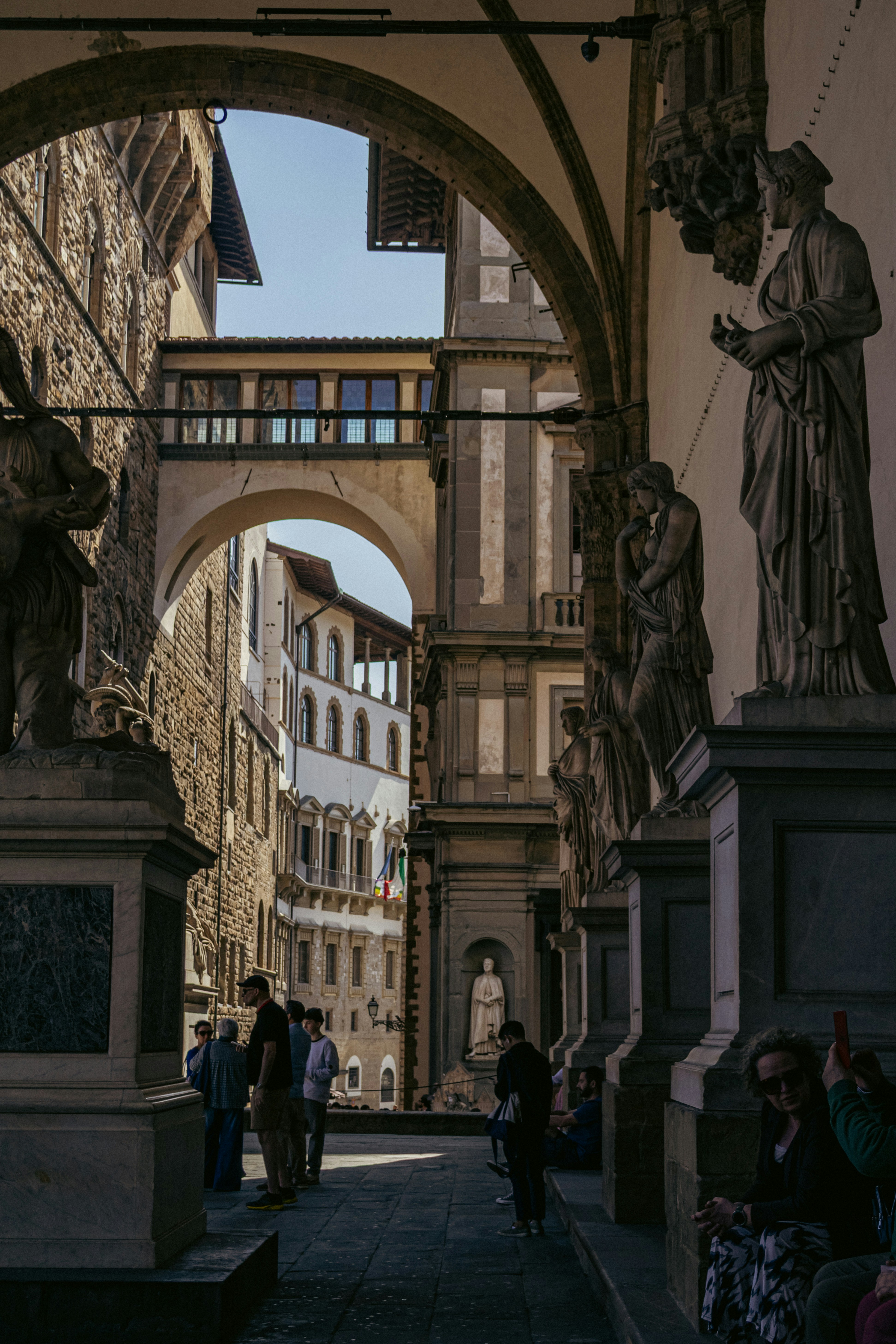 Historic arched passage with classical statues and distant buildings.