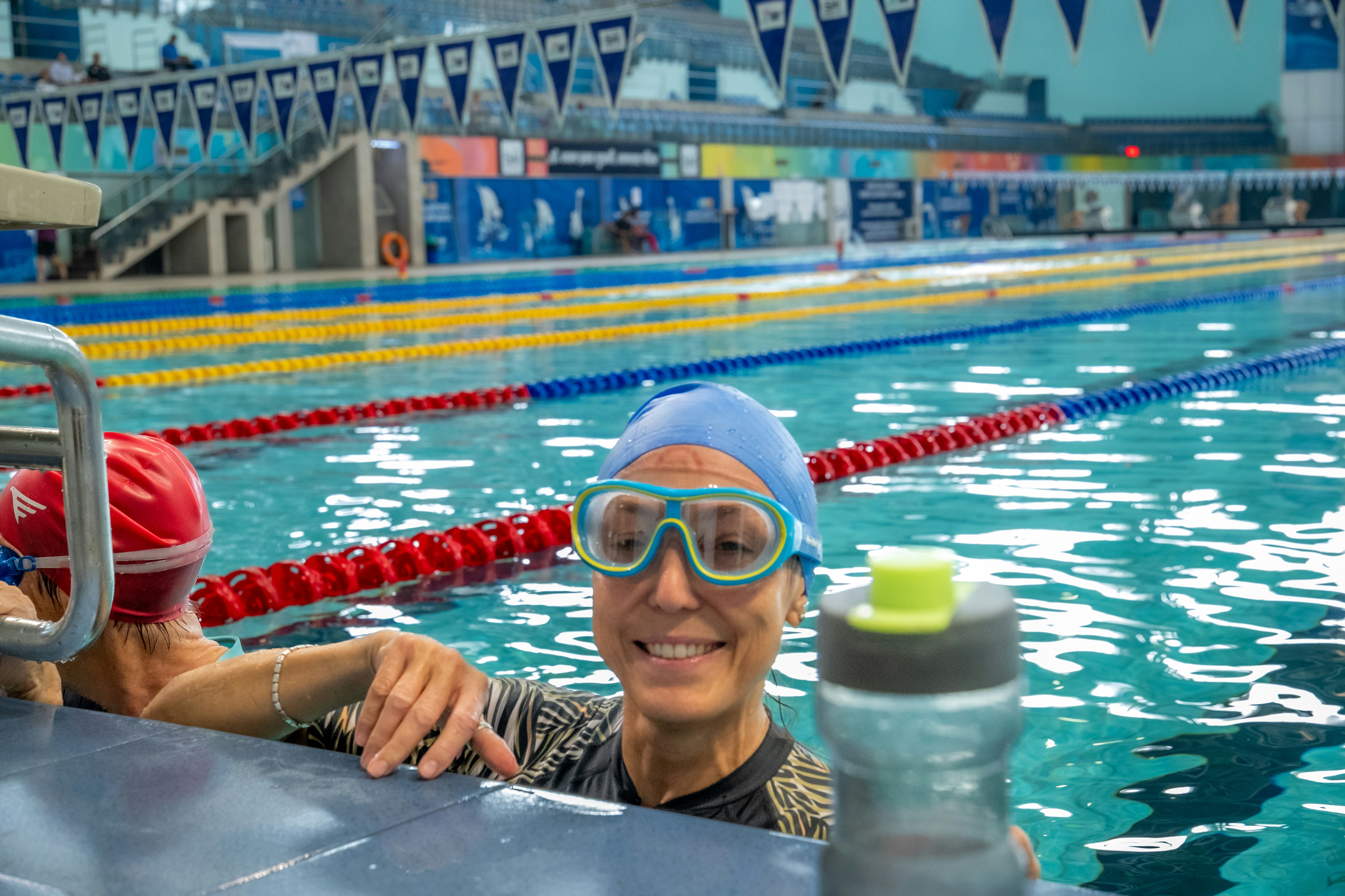 Woman in blue cap and goggles smiles in swimming pool.