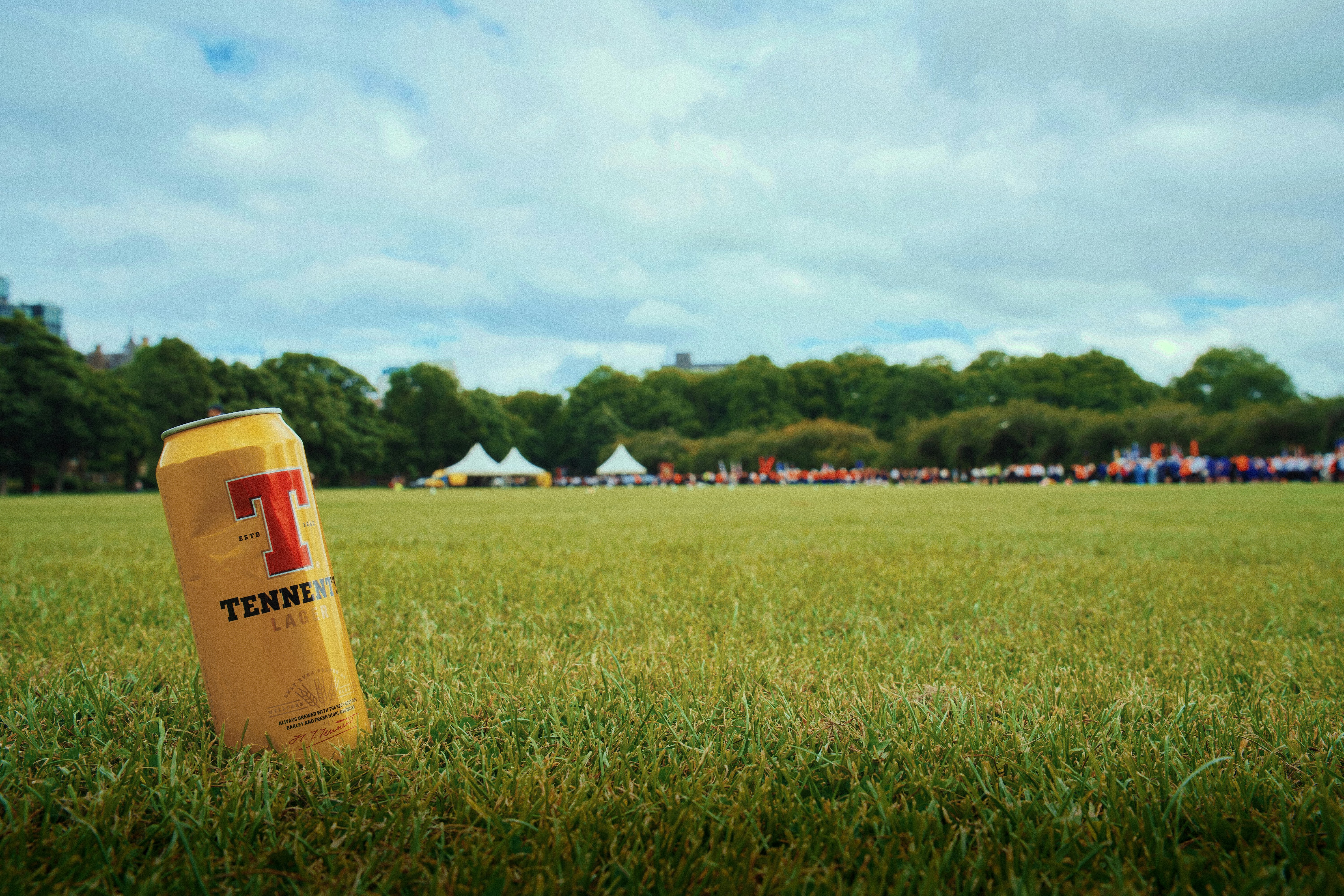 Tennent's can in green field with tents and trees.