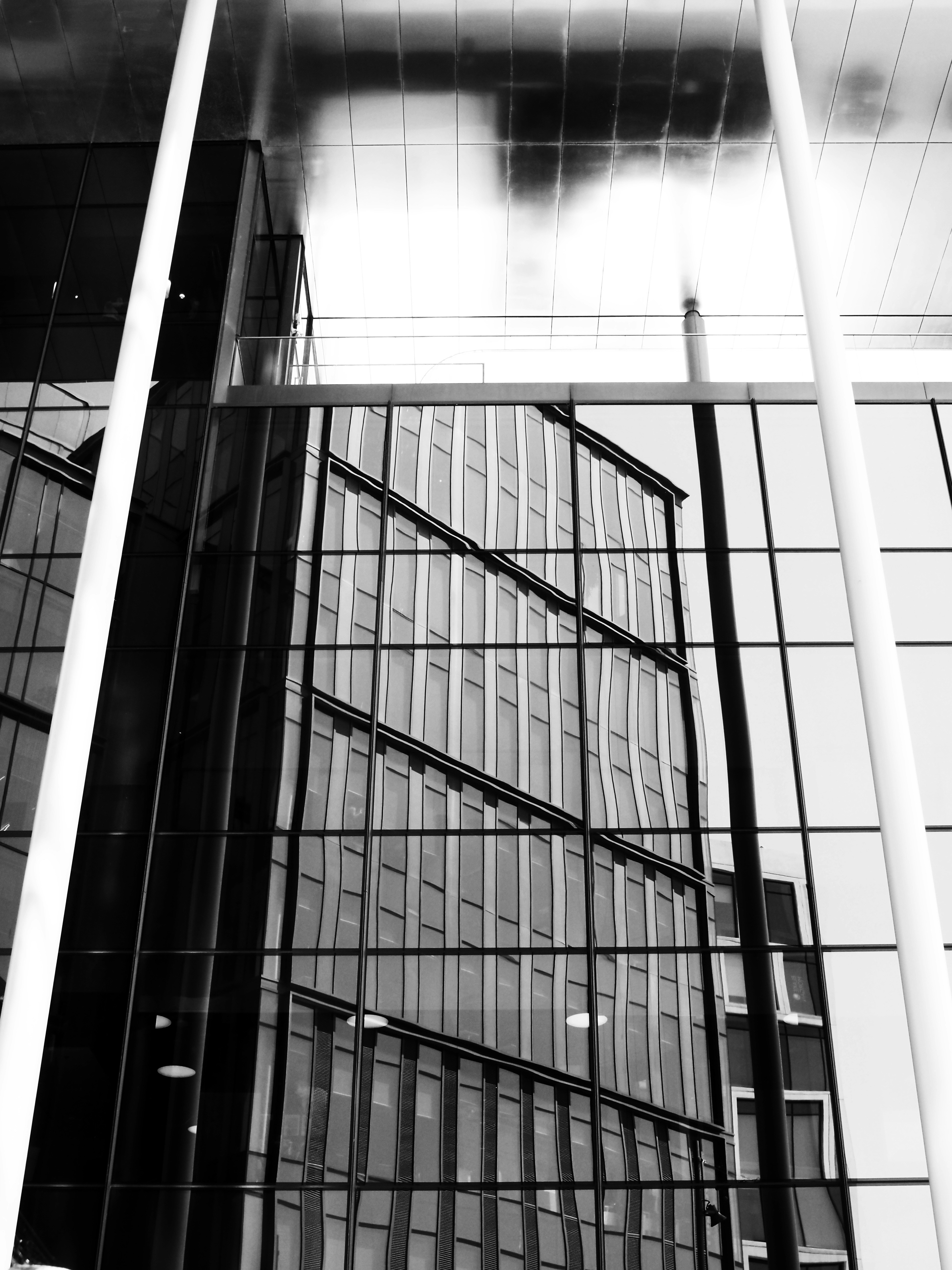 Modern building facade reflecting another building and cloudy sky.