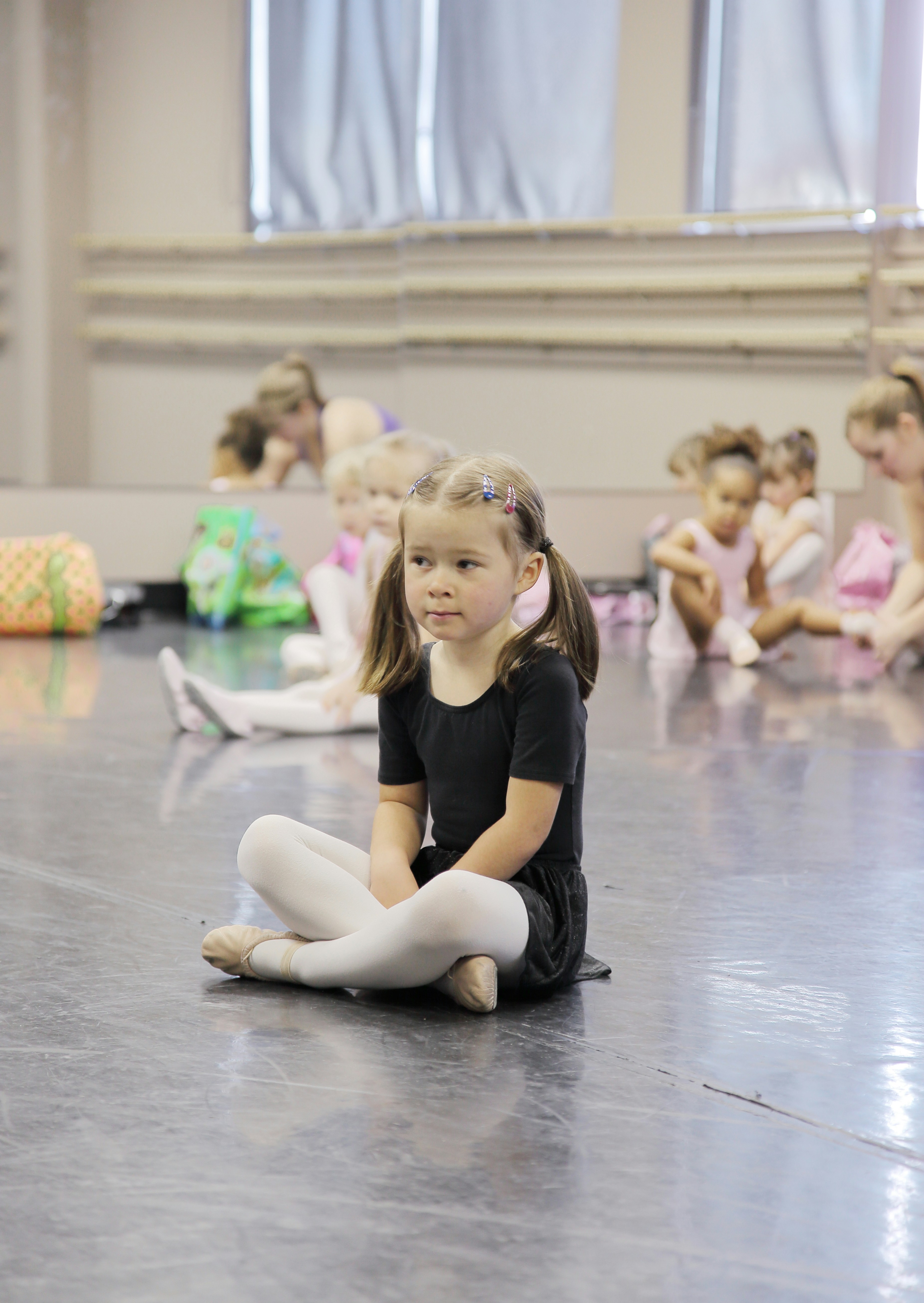 Young girl in ballet attire sitting on studio floor.