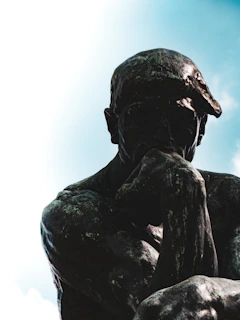 A bronze statue of the thinker against a blue sky.