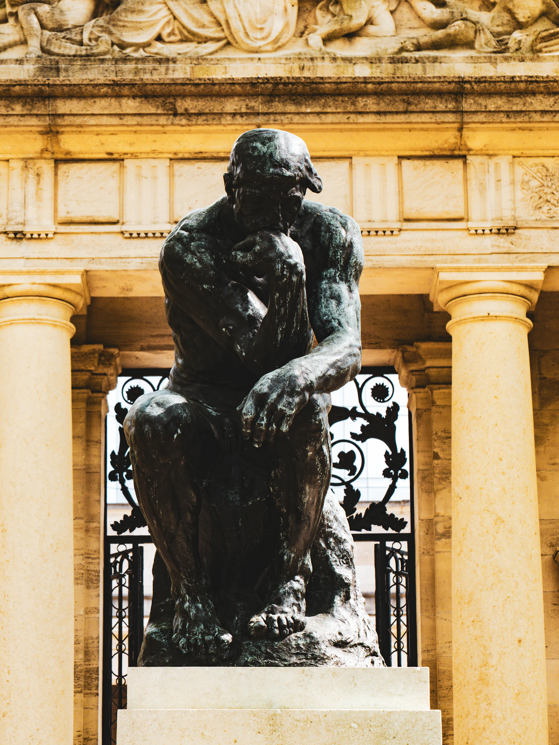 Bronze statue of "the thinker" against classical architecture.