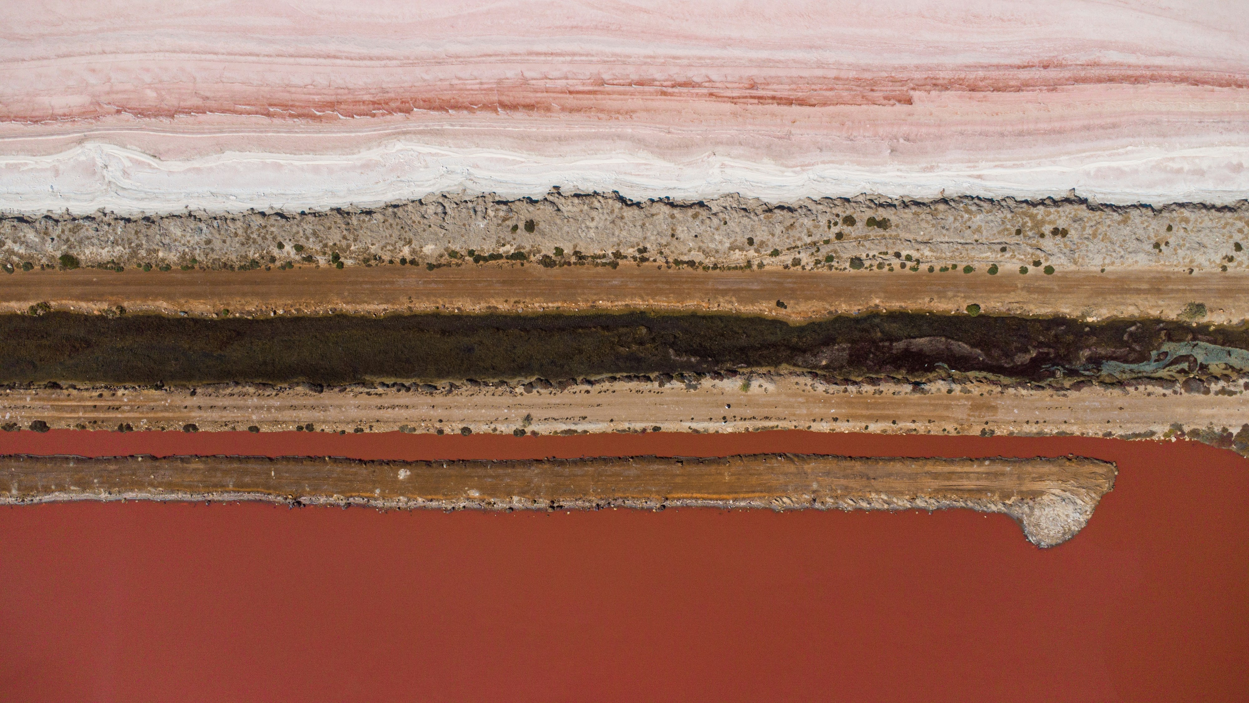 Vibrant pink water meets layered mineral deposits.