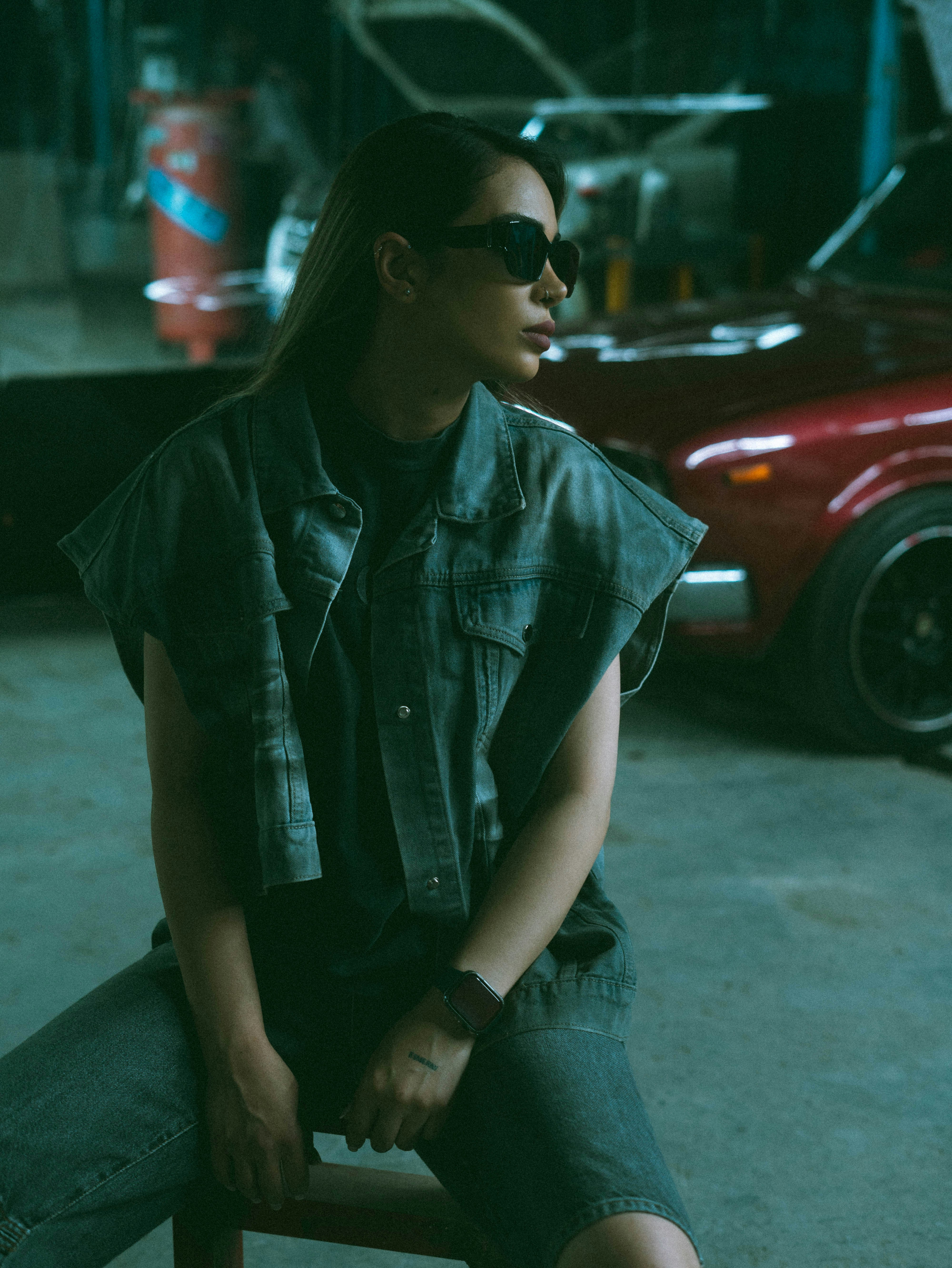 Mulher de óculos escuros e colete jeans sentada em uma garagem.