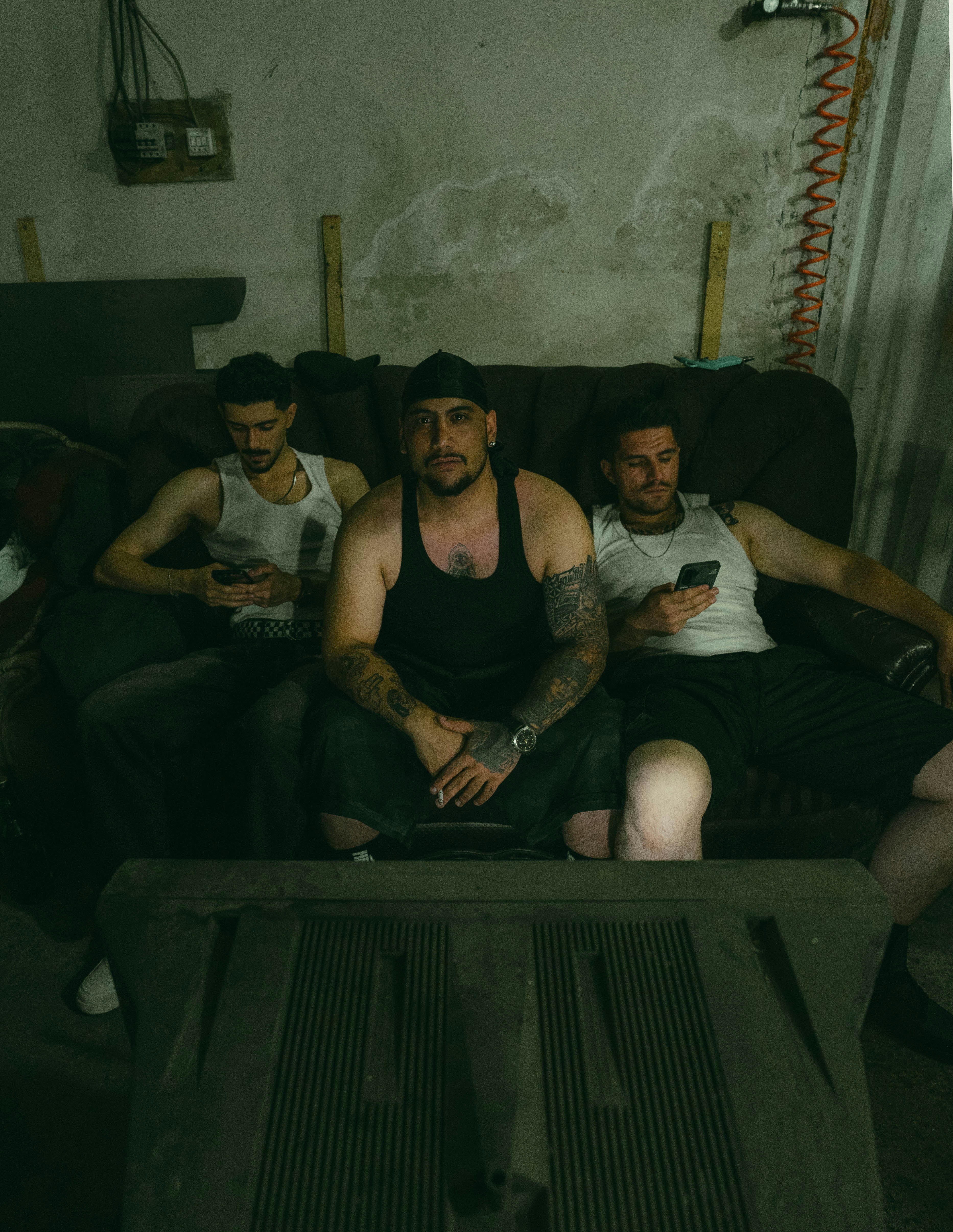 Três homens sentados em um sofá em um quarto rústico.