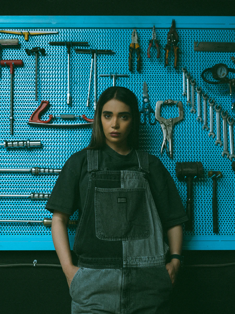 Leila, founder of Pegboard, in denim overalls in front of a blue pegboard full of tools