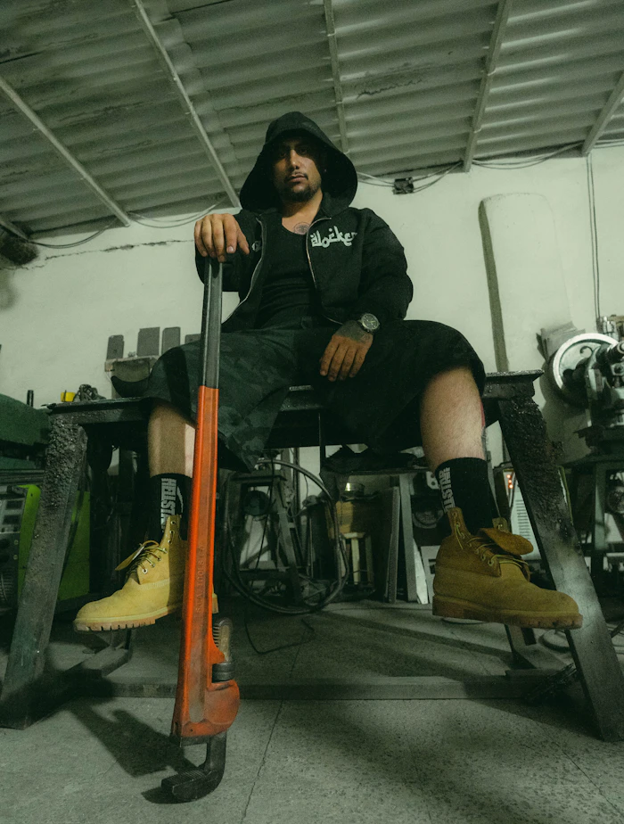 Theo sitting on a workbench holding a big pipe wrench
