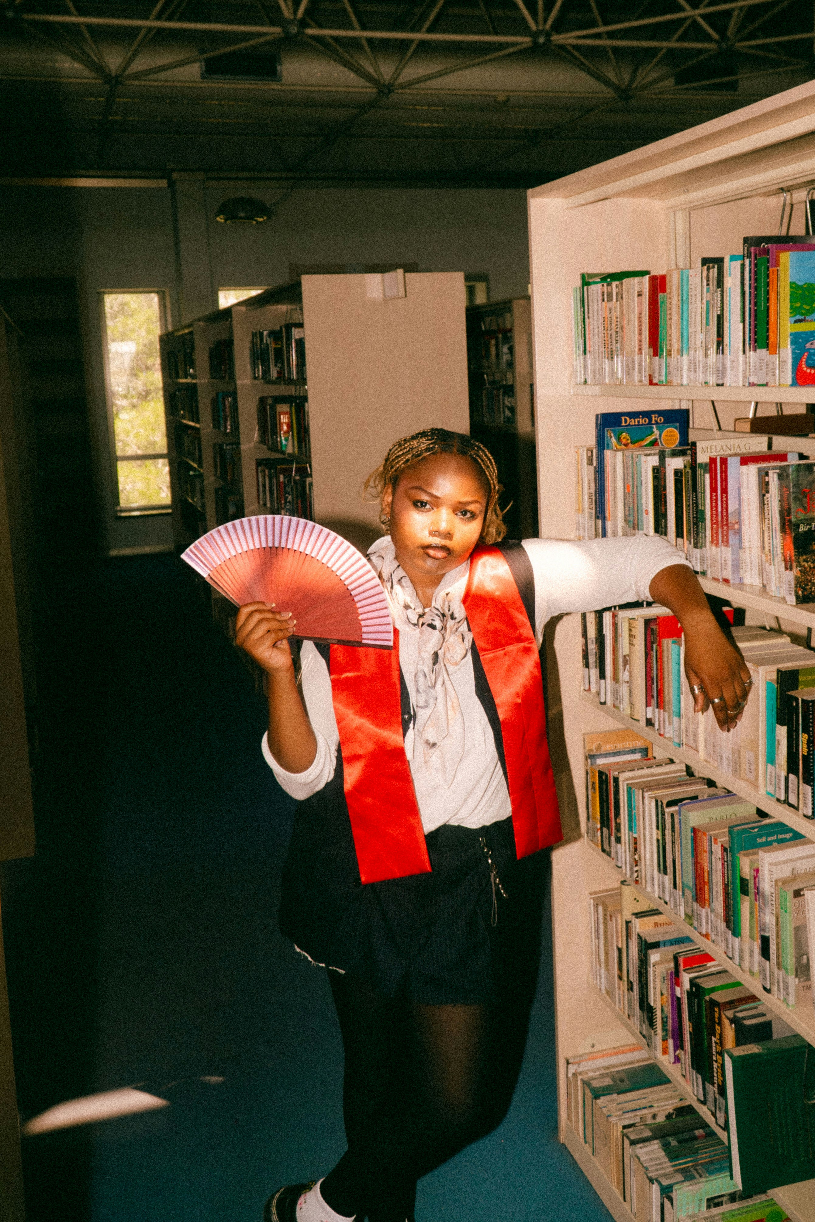図書館の本棚に寄りかかっている赤い扇子を持つ人物