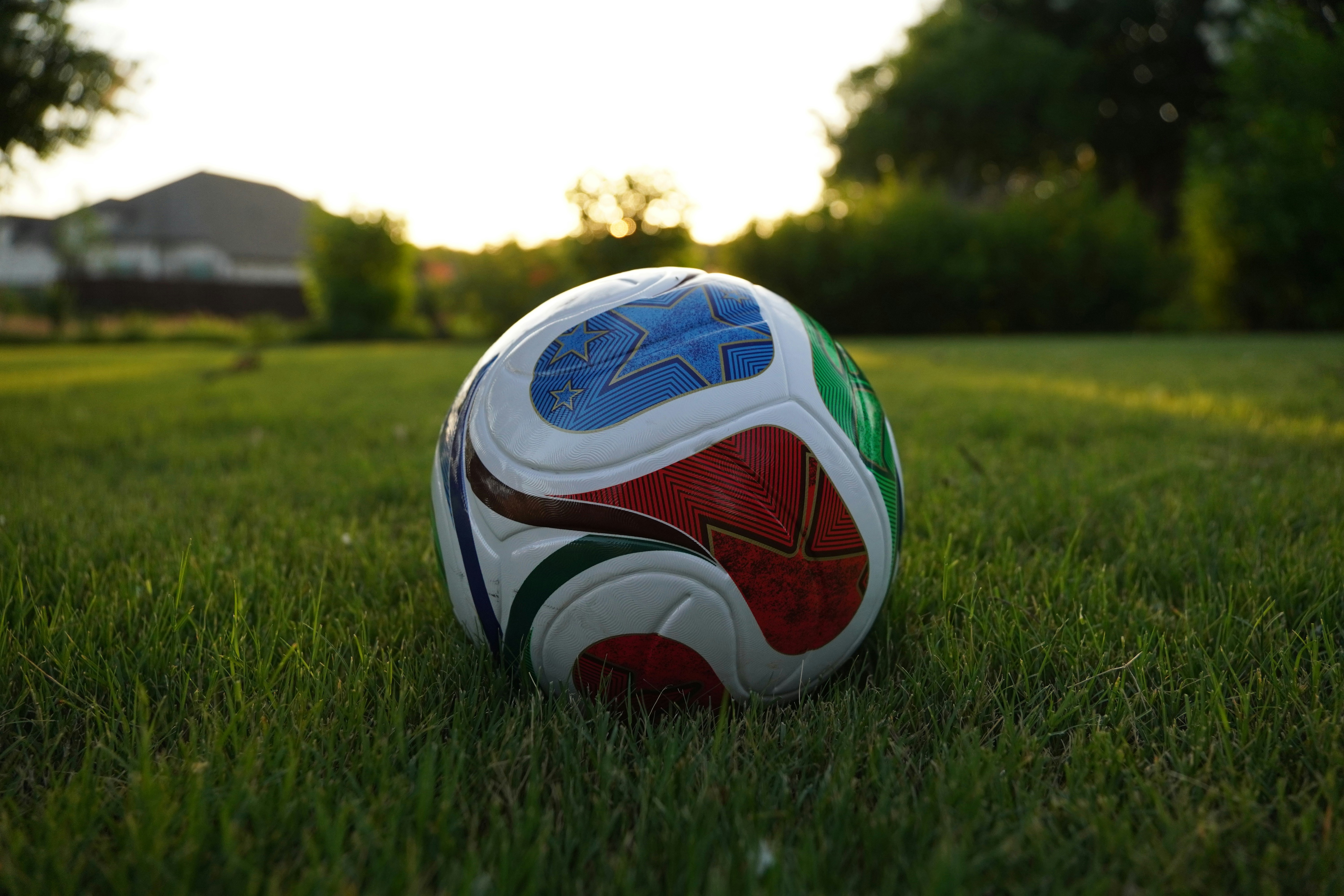 A colorful soccer ball rests on green grass at sunset.