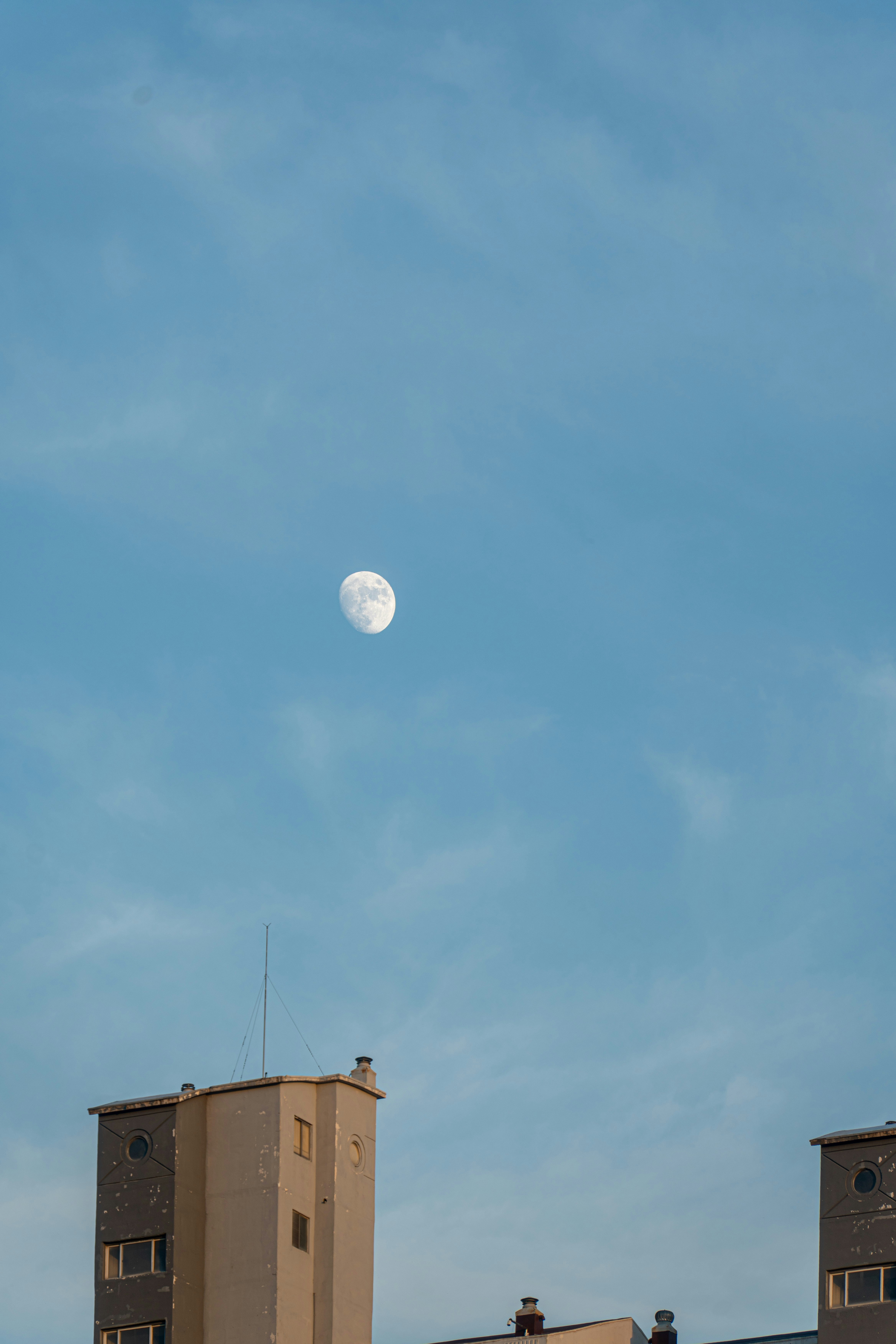 Bright moon in clear blue sky above urban buildings