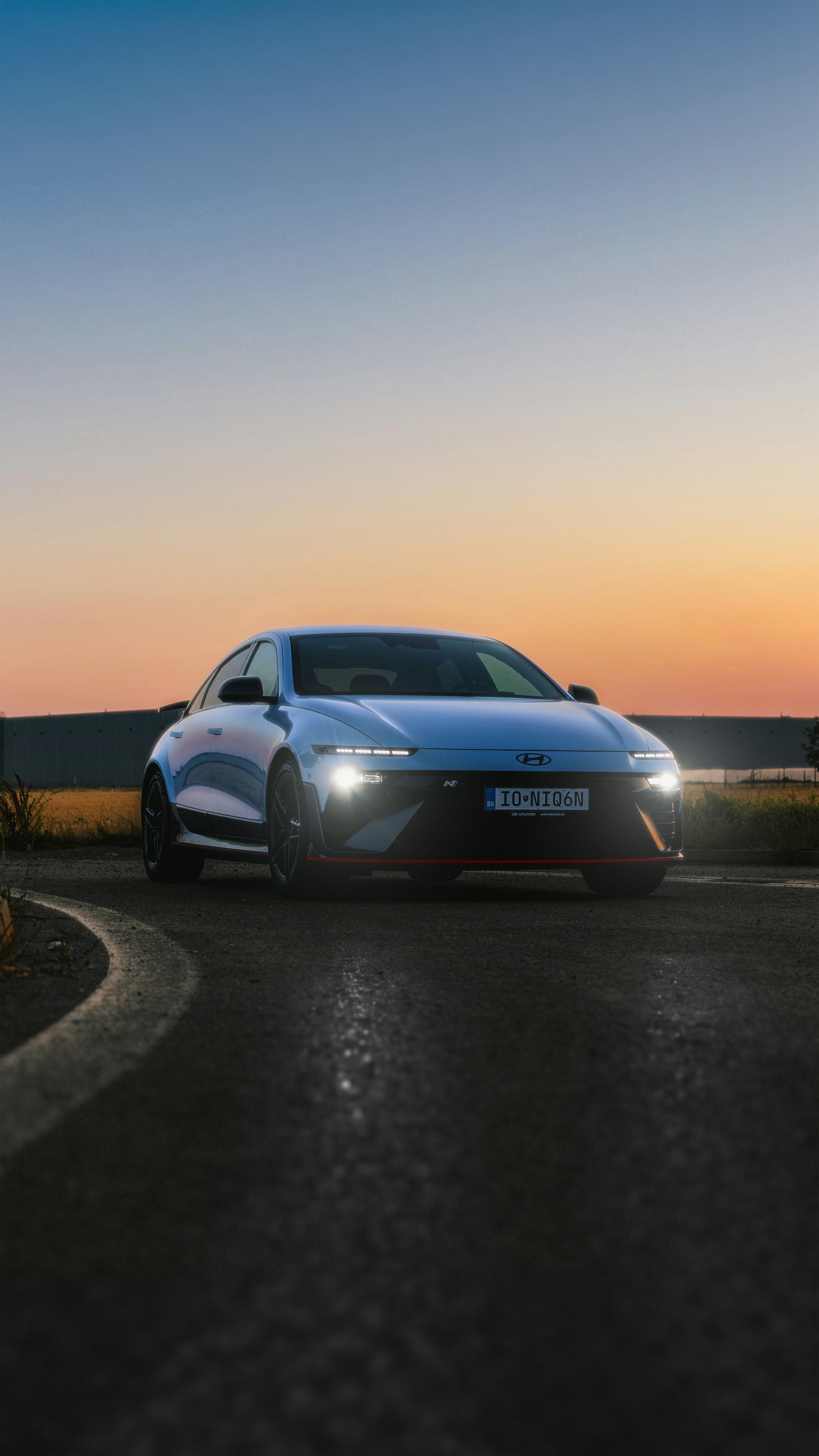 Modern car with bright headlights on a road at sunset.