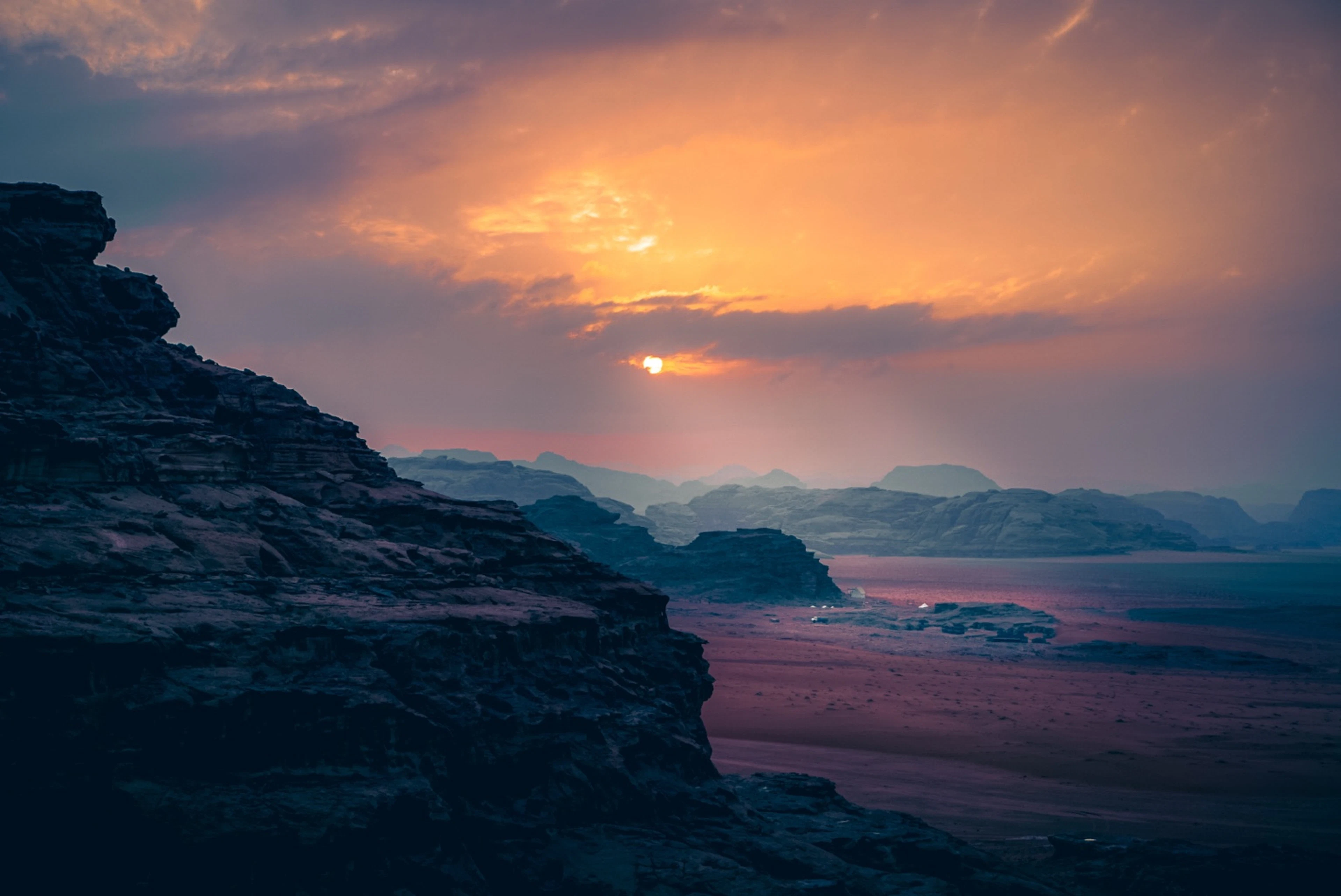 Sunset over sandstone cliffs and a wide desert valley in Wadi Rum