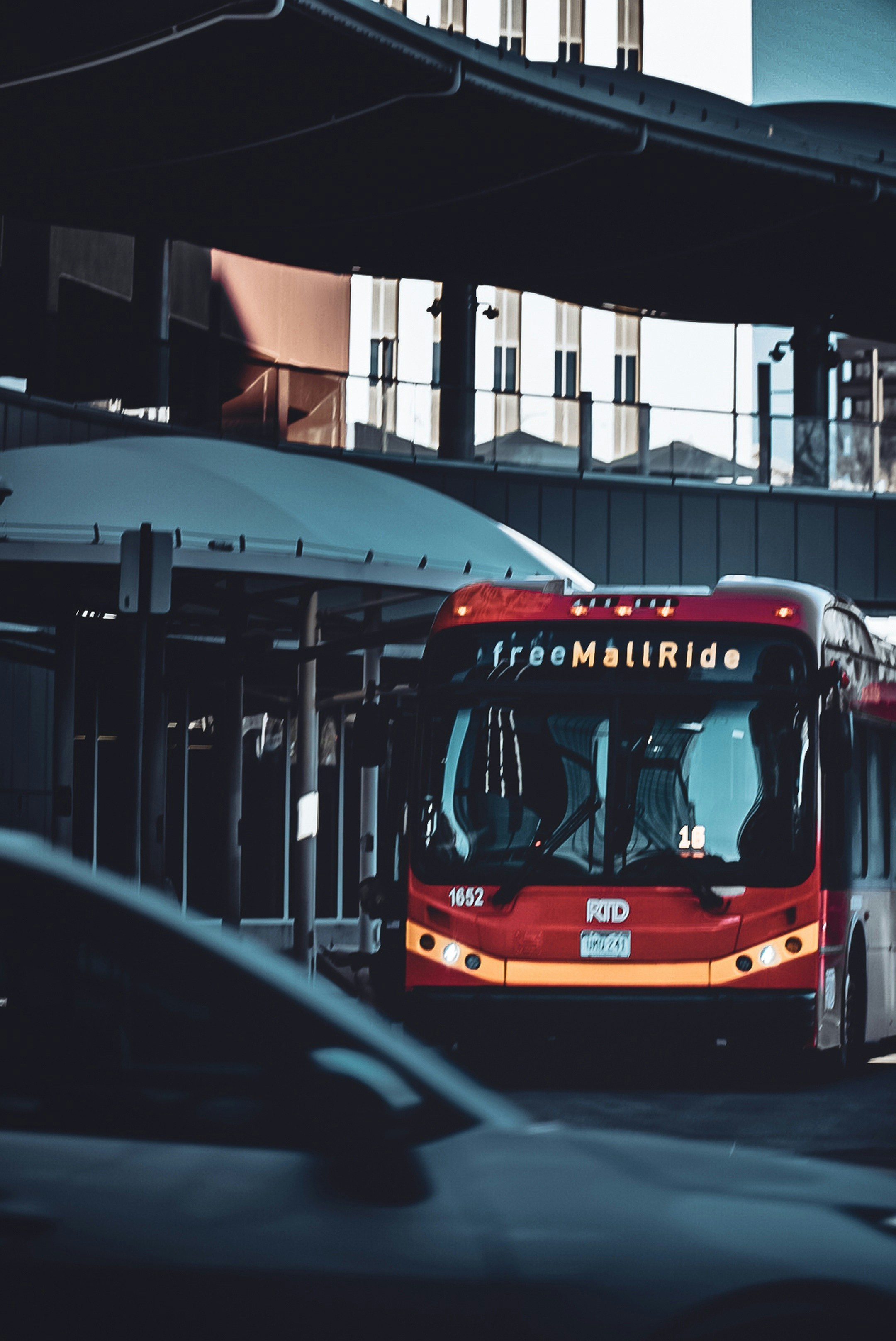 MallRide Close-Up: A Denver Free MallRide bus pulls through the city, framed tightly by traffic, shadows, and downtown transit architecture.