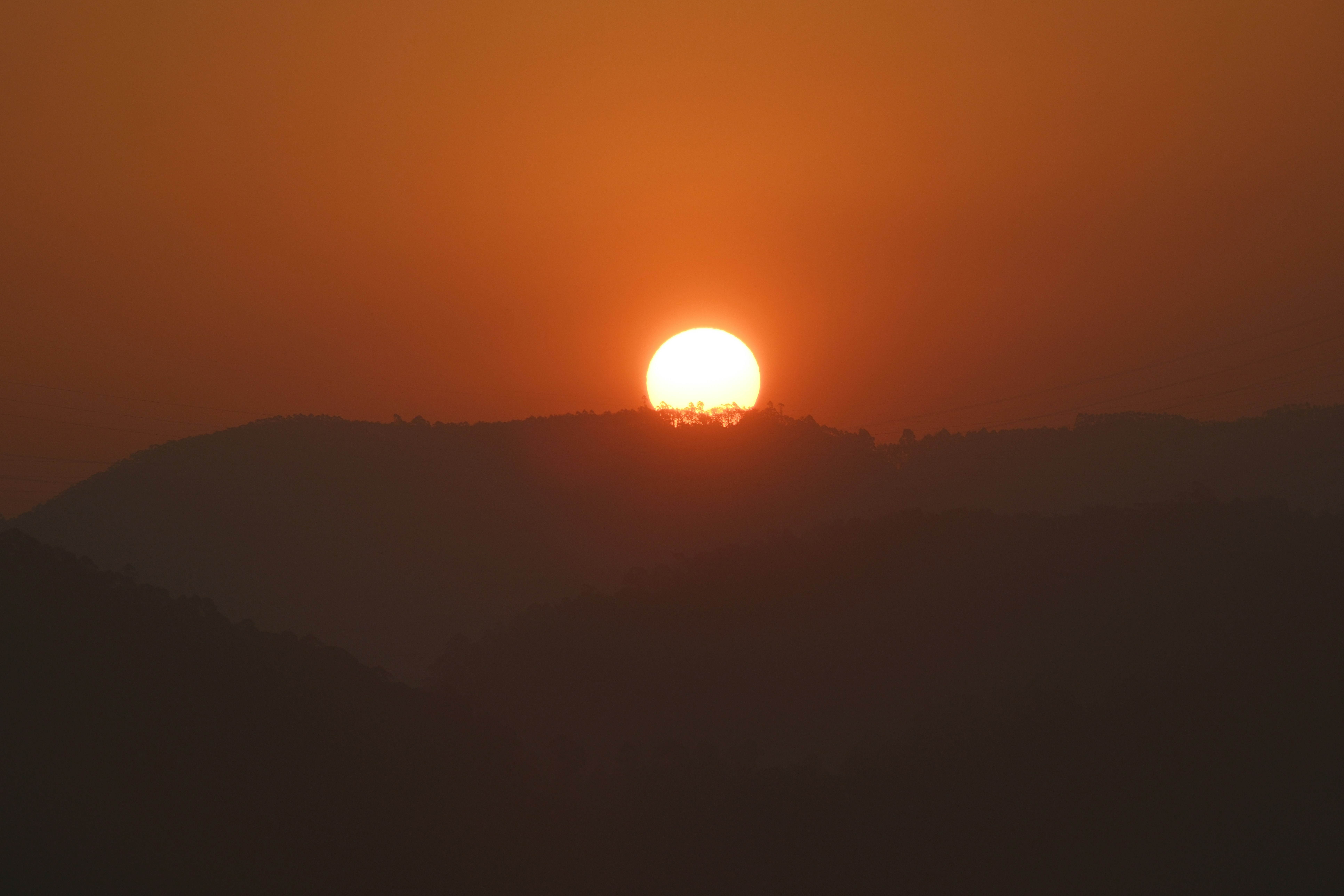 A bright orange sun sets behind dark hills.