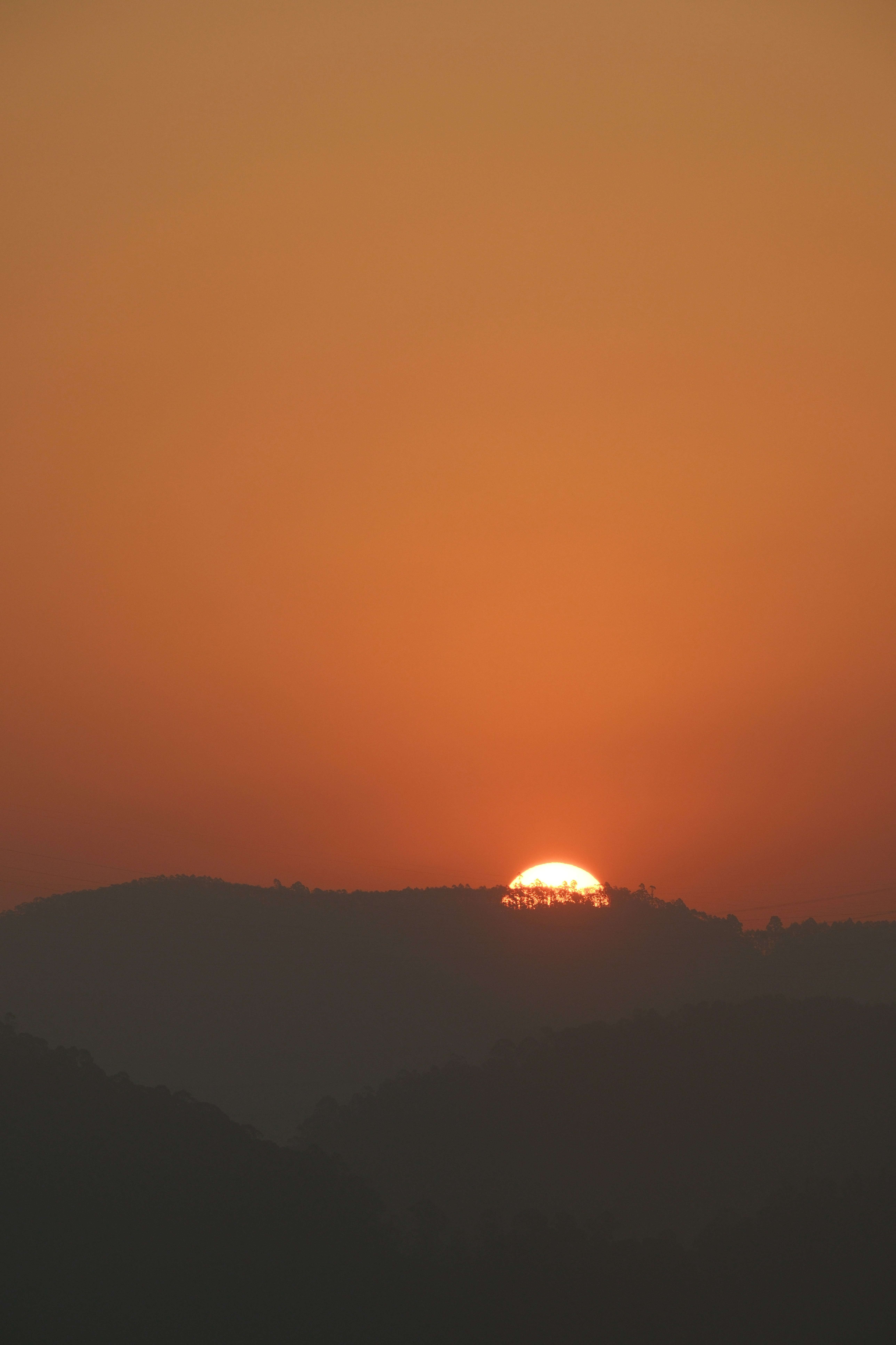 The sun setting behind hills with an orange sky.