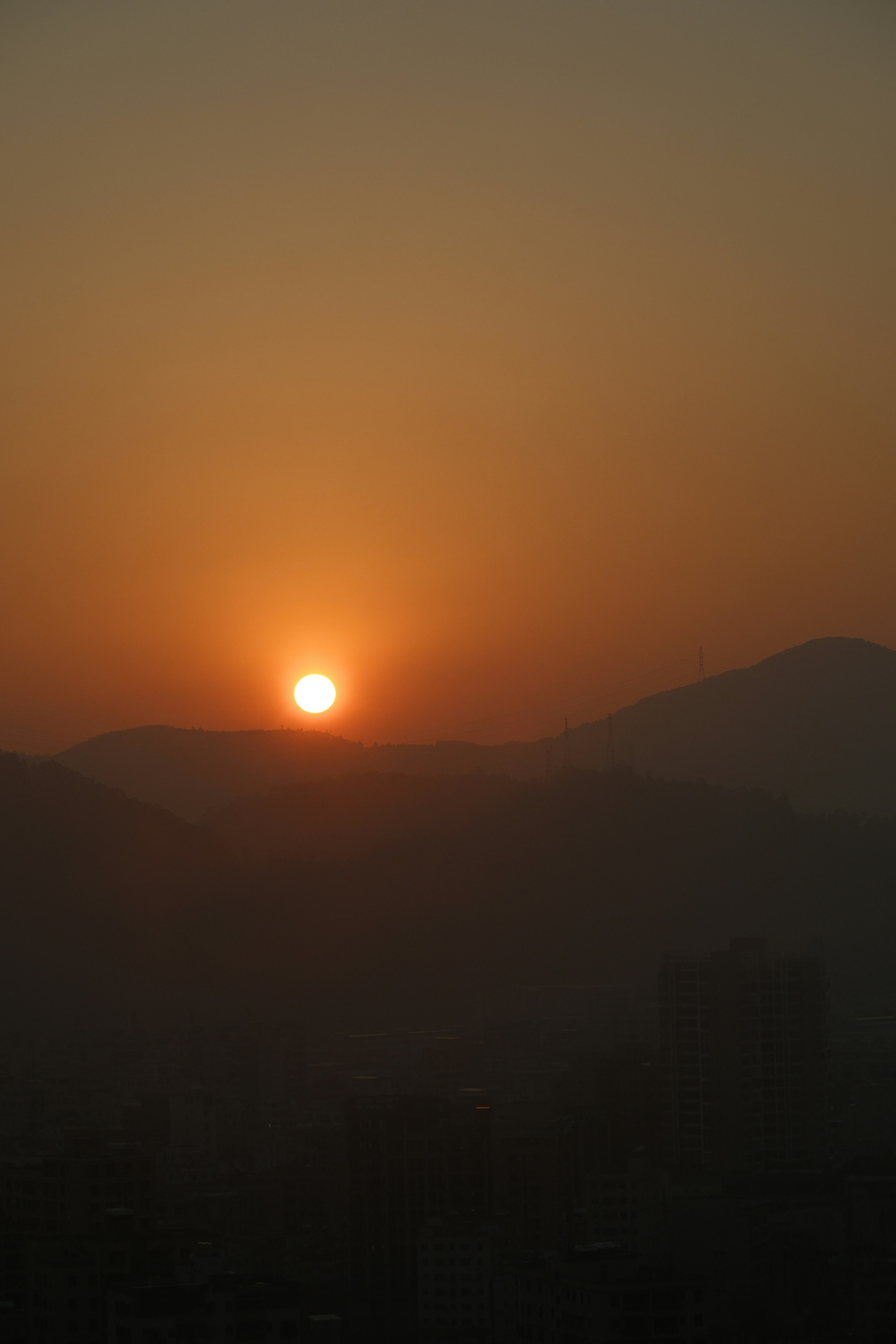 Vibrant orange sunset over dark mountains and hazy sky.