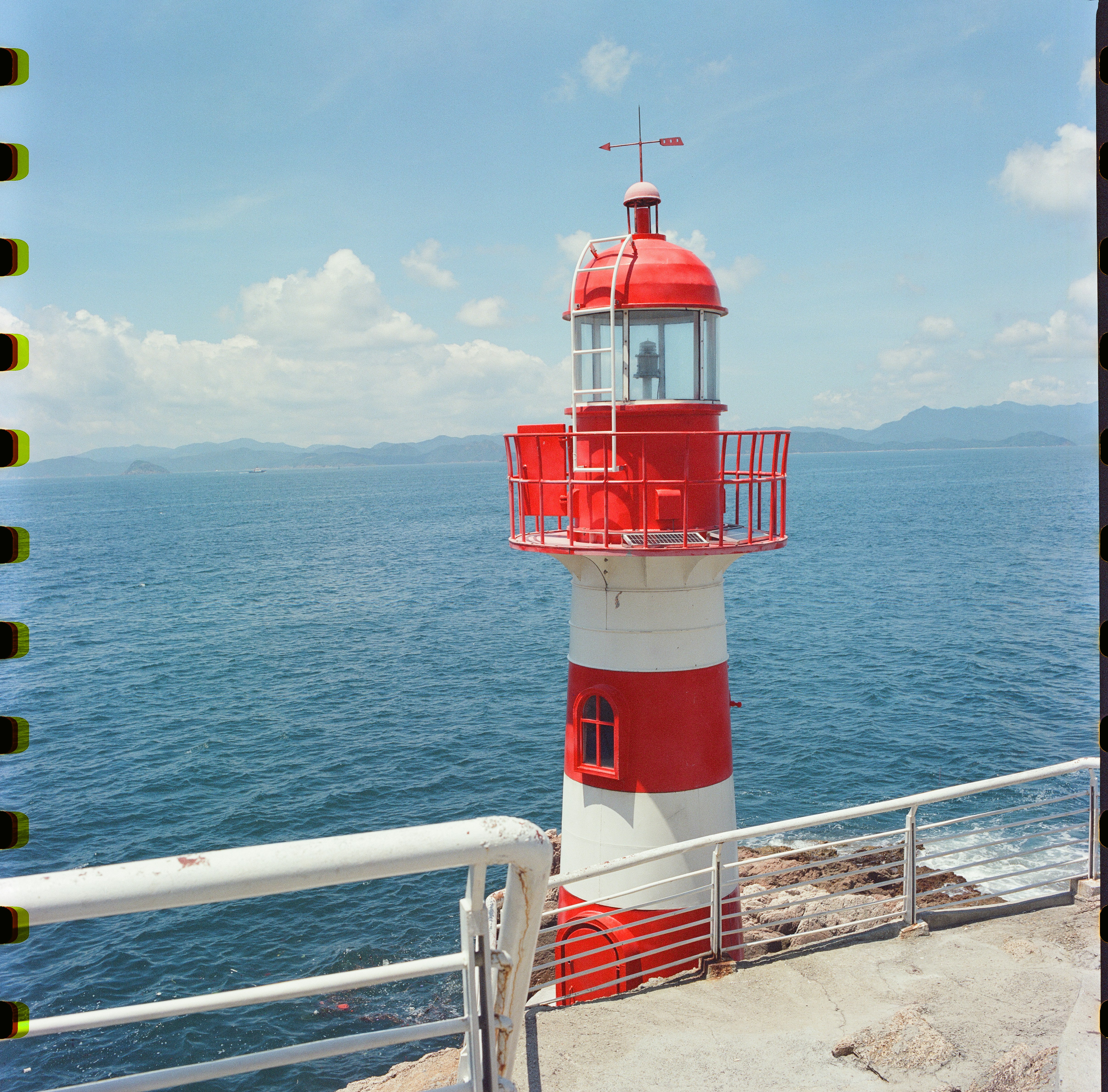 A red and white lighthouse stands by the blue ocean.