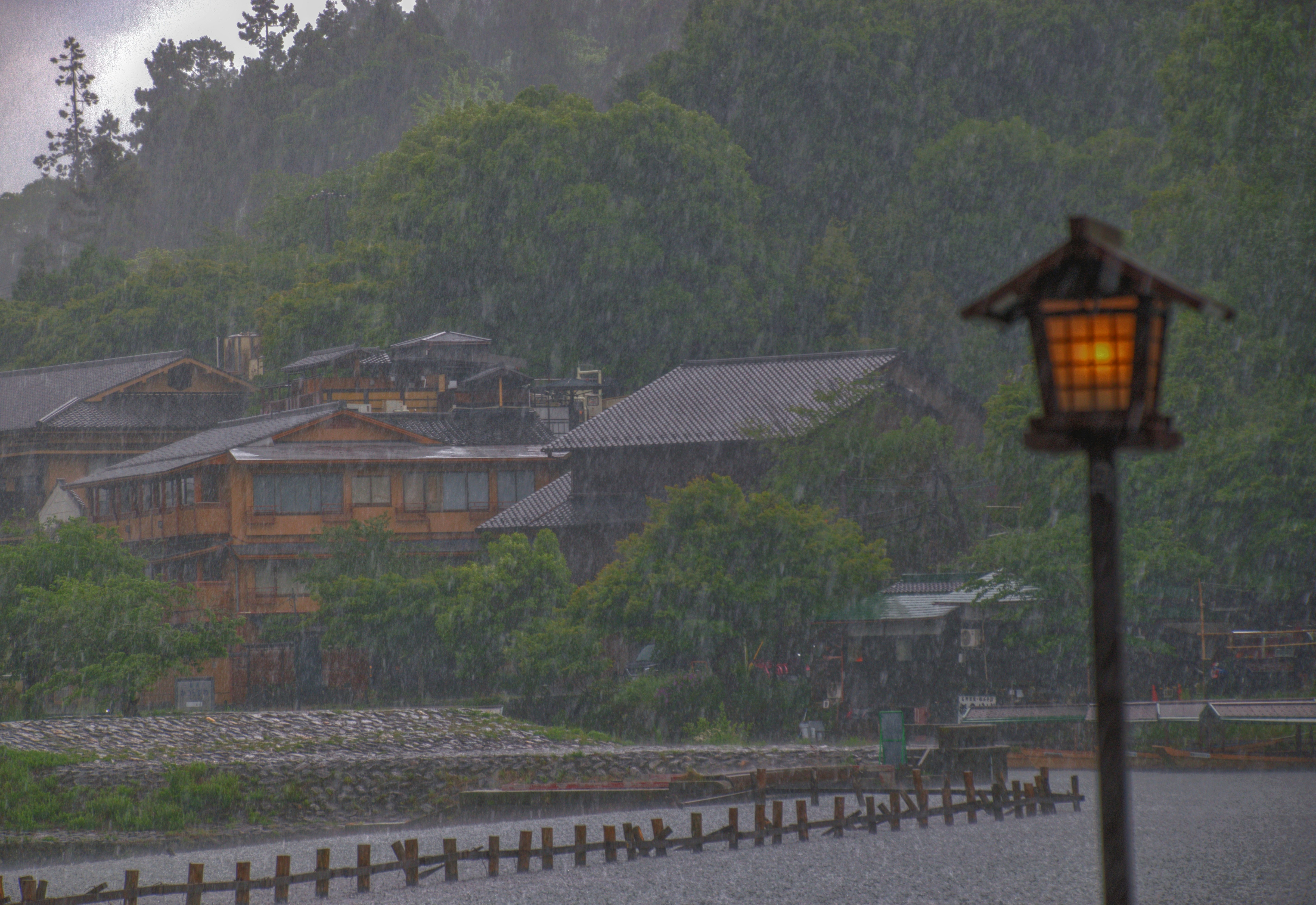 Una linterna encendida se encuentra bajo la lluvia junto a edificios tradicionales