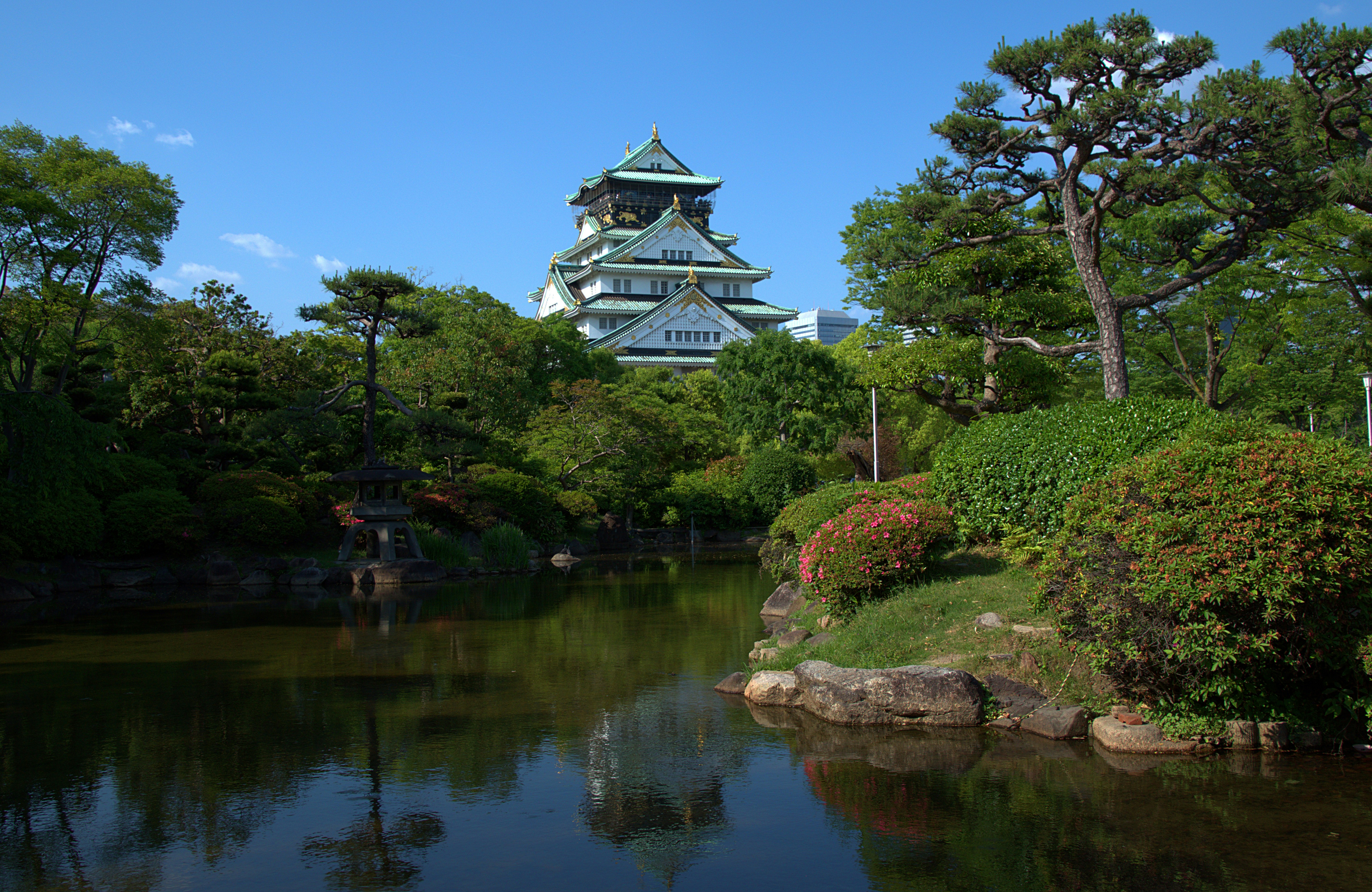 El castillo de Osaka se eleva sobre un estanque sereno y árboles verdes