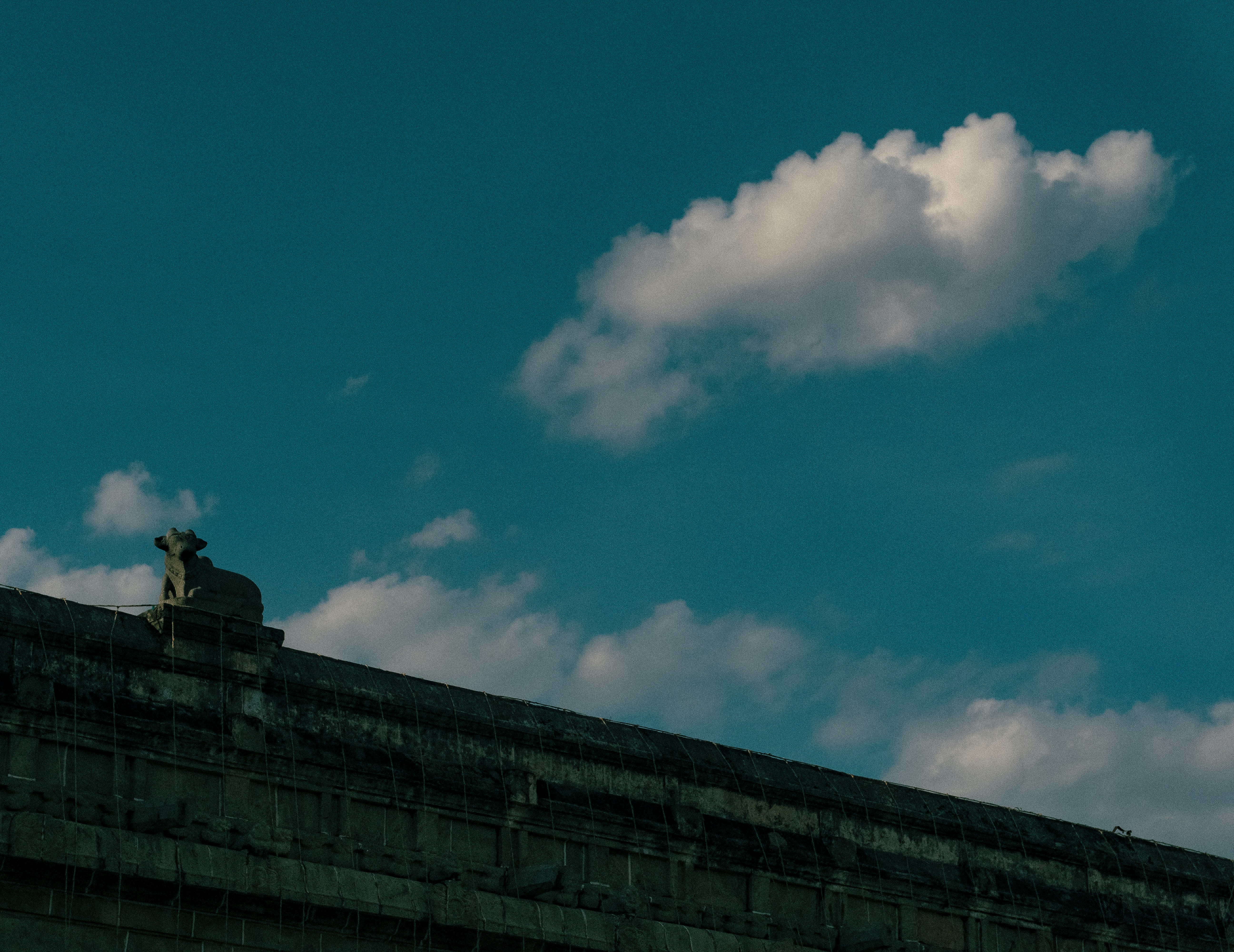 Statue on building roofline against blue sky with a cloud