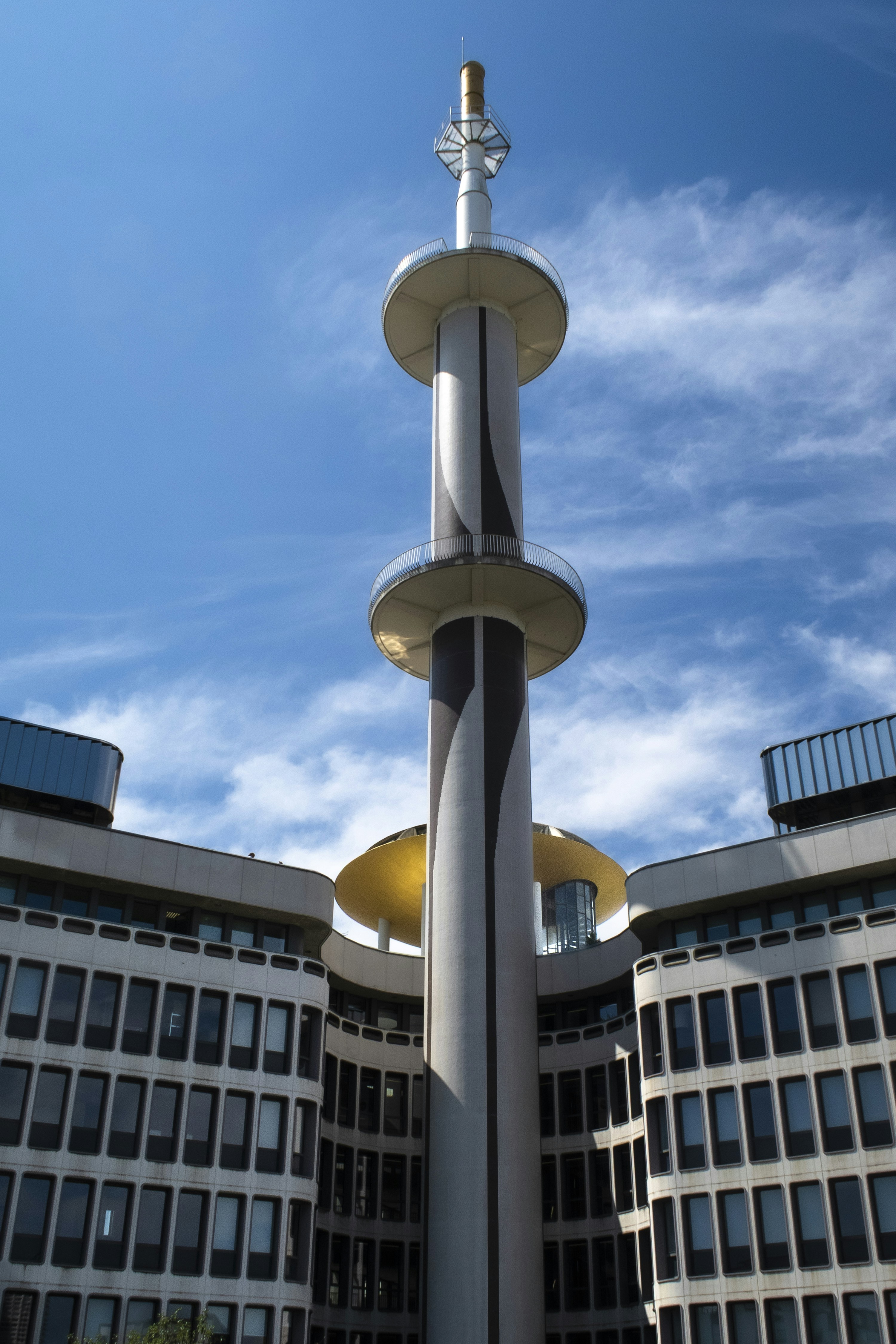 A modern tower with circular platforms rises above a building.