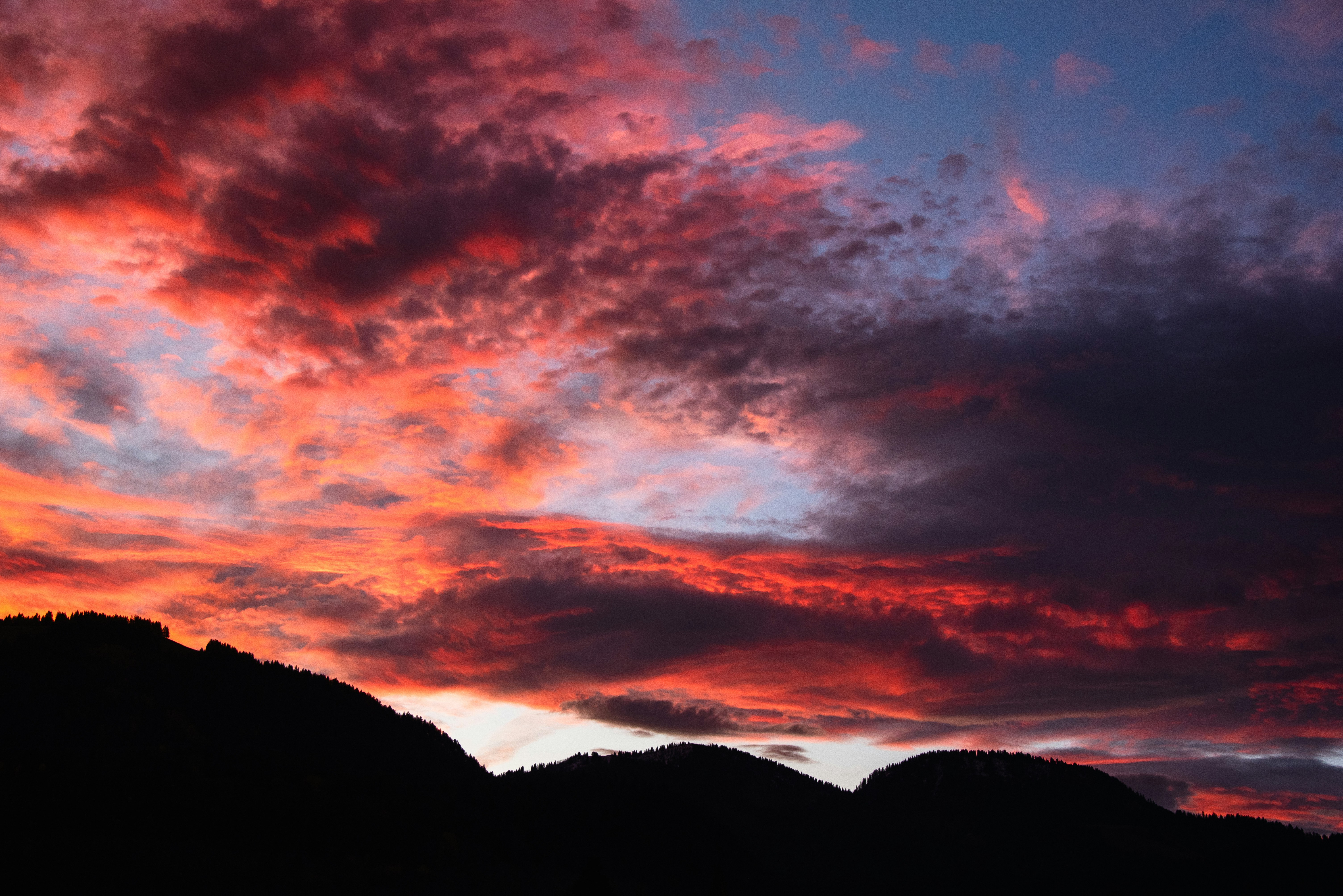 Awan matahari terbenam merah dan oranye cerah di atas siluet gunung yang gelap
